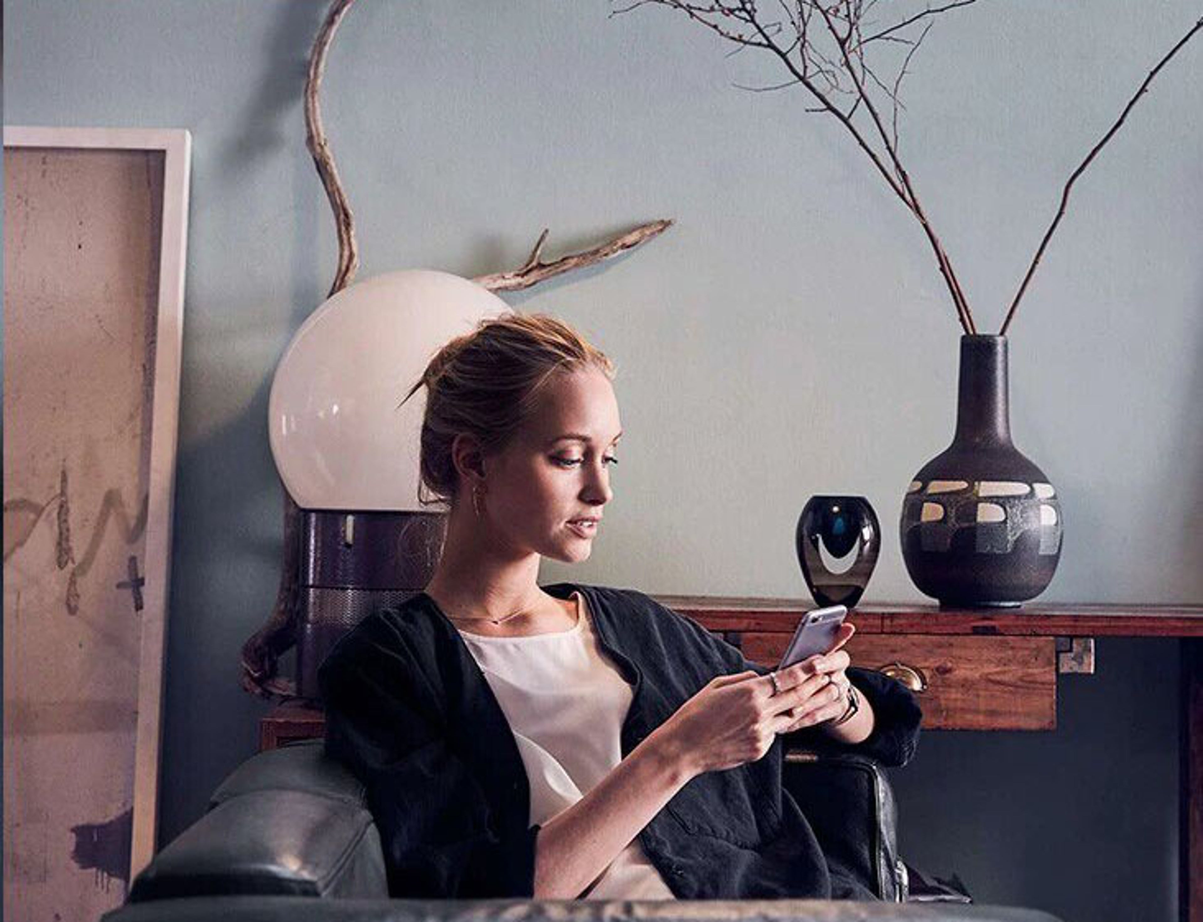 Une femme assise dans un fauteuil confortable regarde son smartphone, dans un espace élégamment décoré avec des éléments de design.