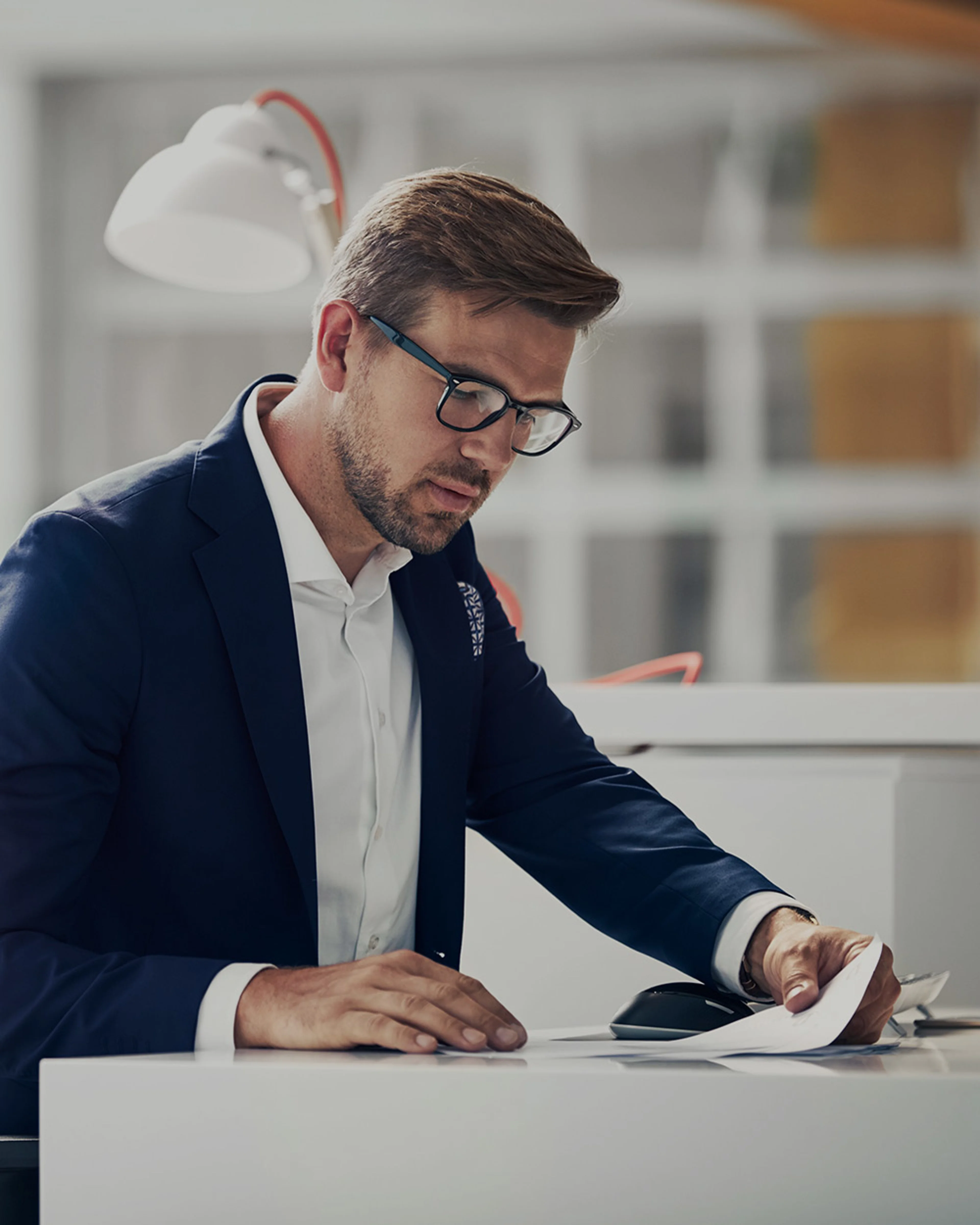 Un homme en costume et lunettes est assis à un bureau et examine des documents.