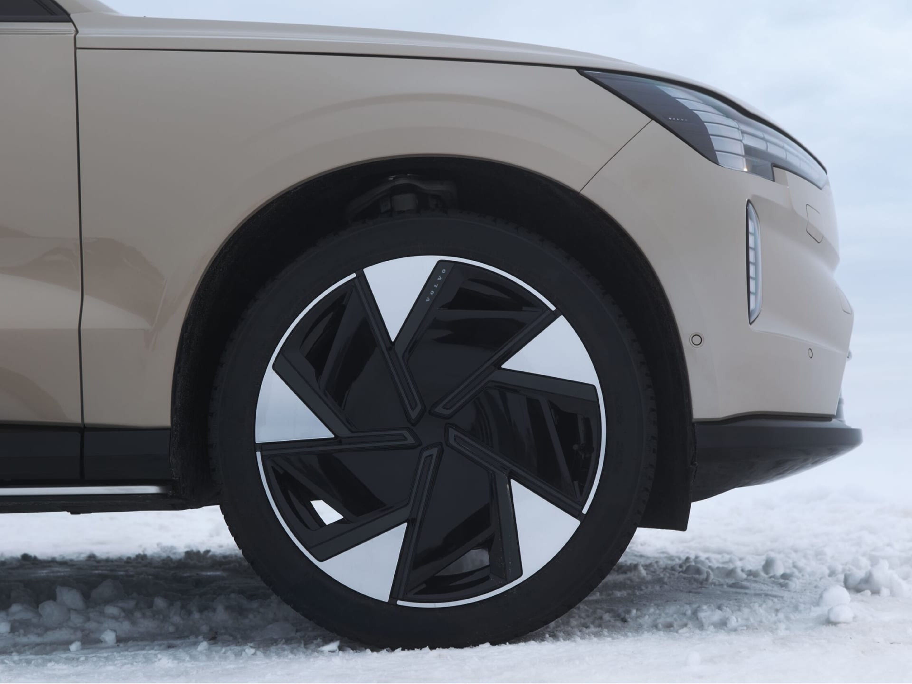 Close-up op wiel van een Volvo EX90 in Sand Dune met complete winterwielenset, geparkeerd op de sneeuw