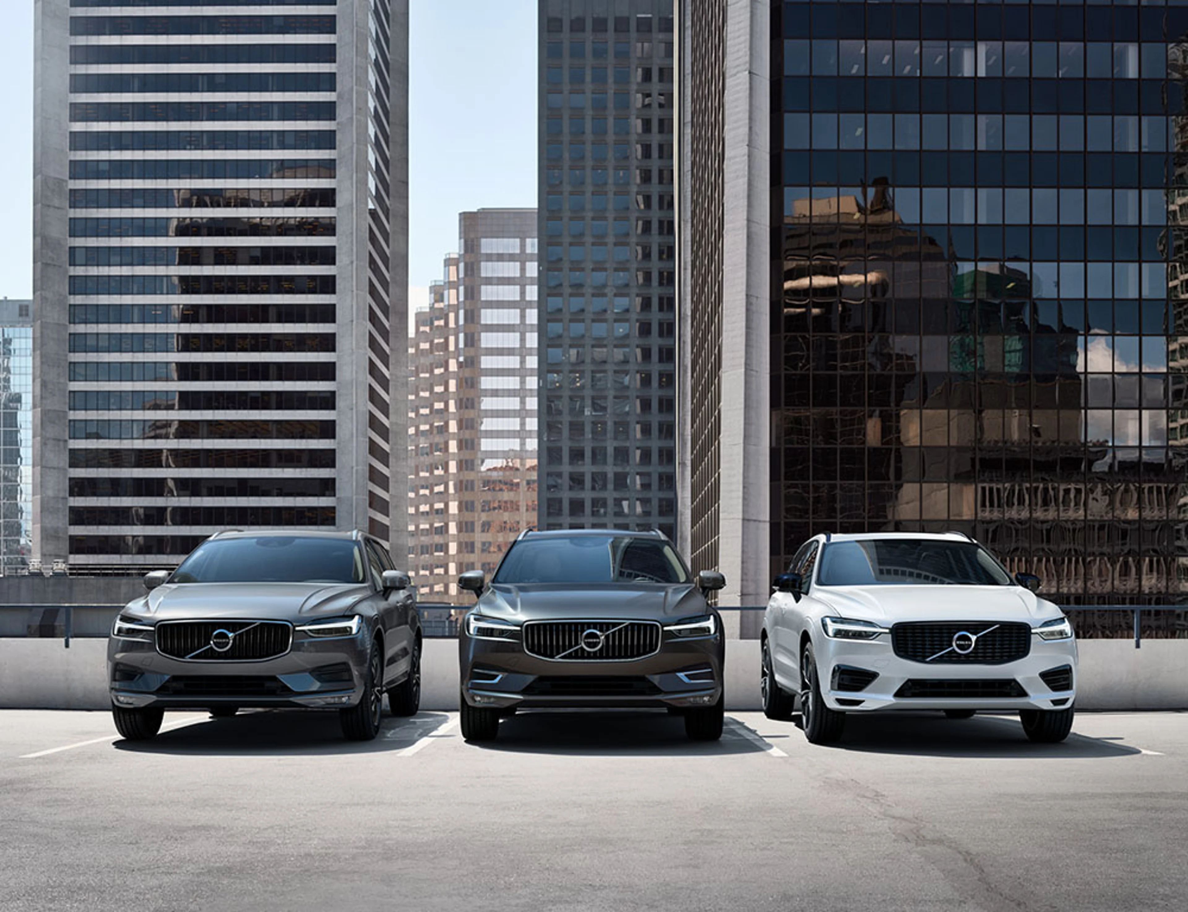 Trois Volvo XC60 garées sur un toit avec des gratte-ciels en arrière-plan.