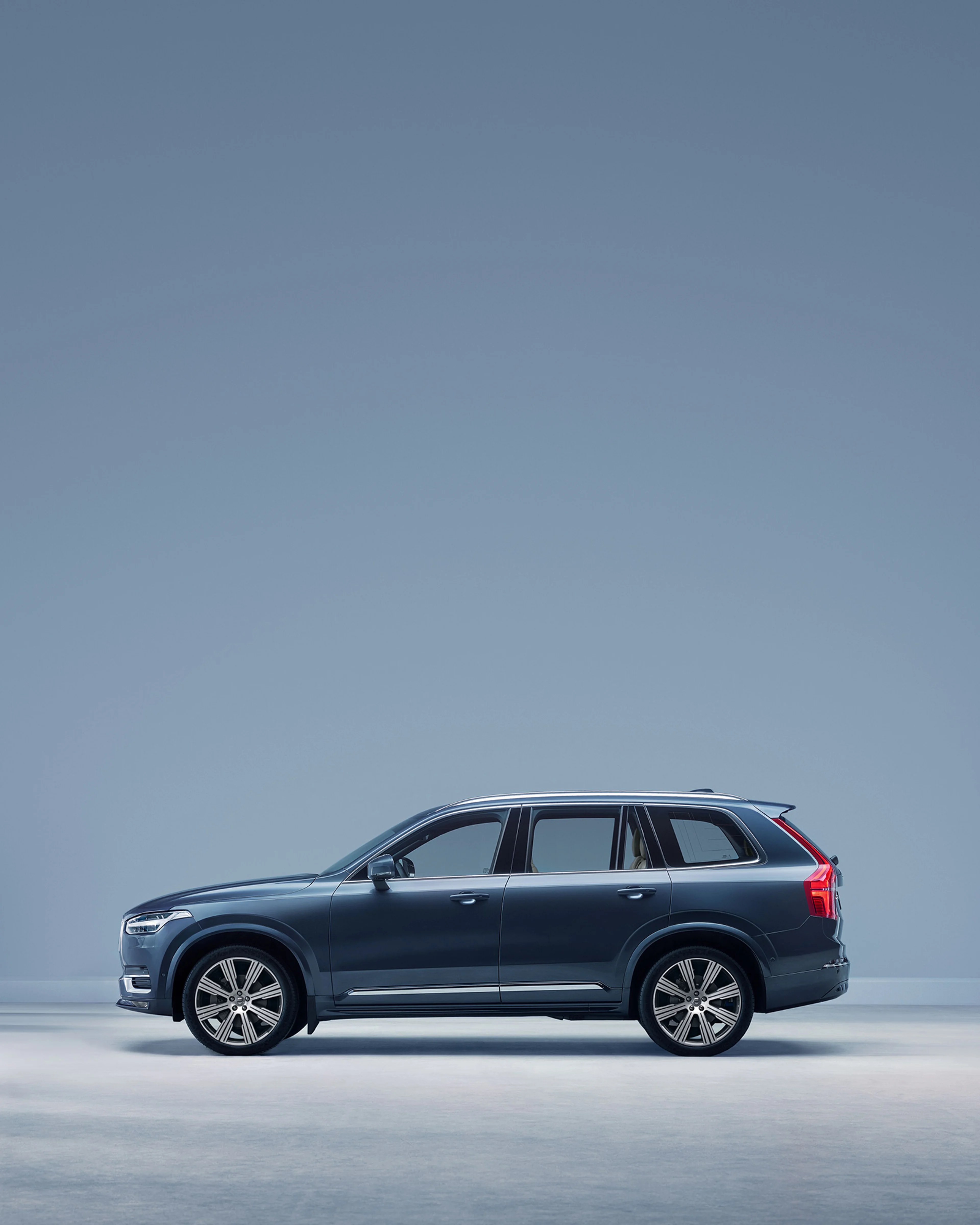 Donkere Volvo XC90 geparkeerd tegen een blauwe achtergrond