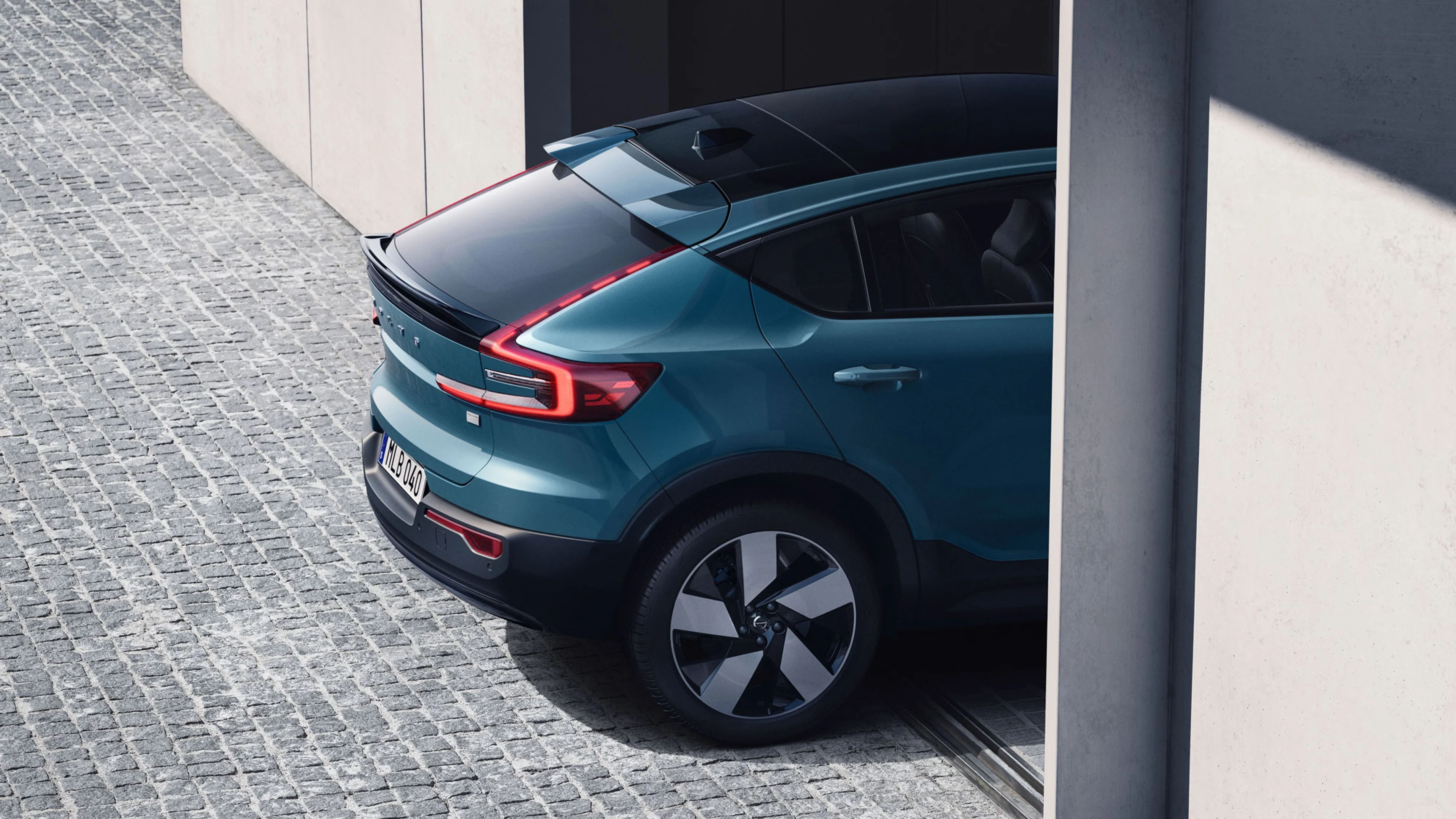 Vue arrière d’une Volvo XC40 bleue garée sur pavés, à côté de murs en béton modernes