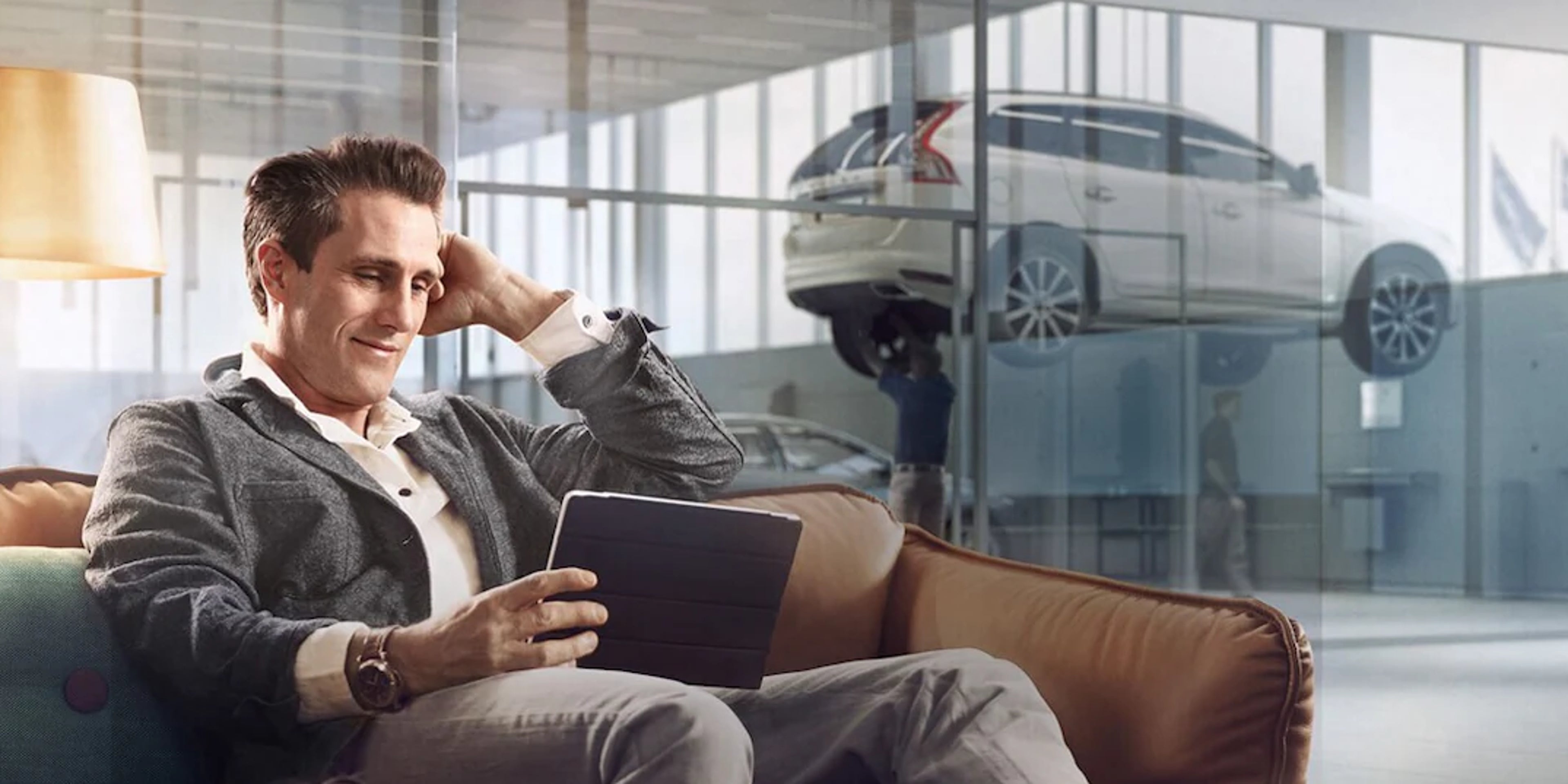 Ein Mann sitzt auf einem beigen Sofa und schaut auf Tablet, welches er in der Hand hält.