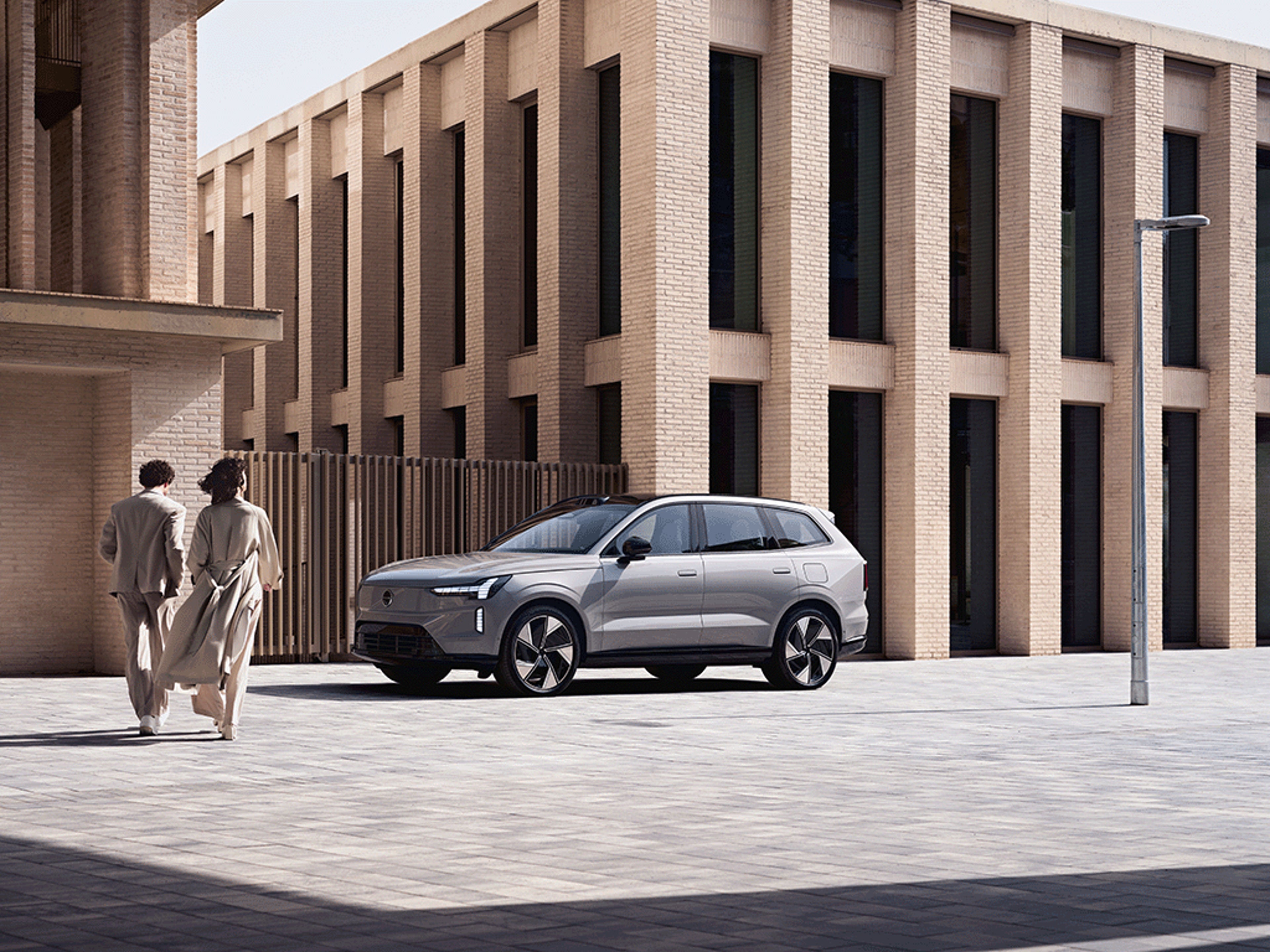 Zwei Personen laufen auf einen Volvo EX90 zu.