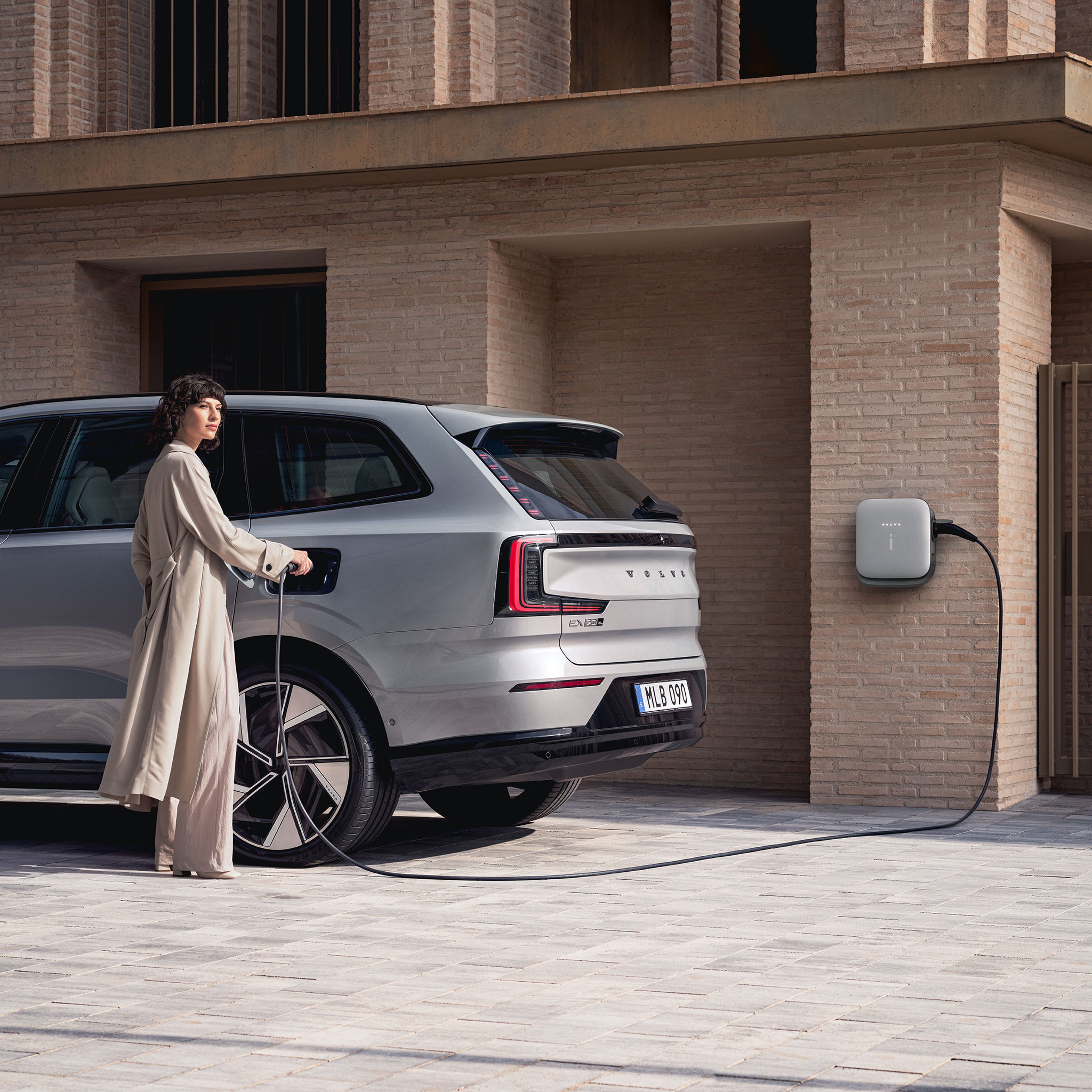 Nainen kytkee Vapour Grey -väristä Volvo EX90 täyssähköautoa lataukseen.