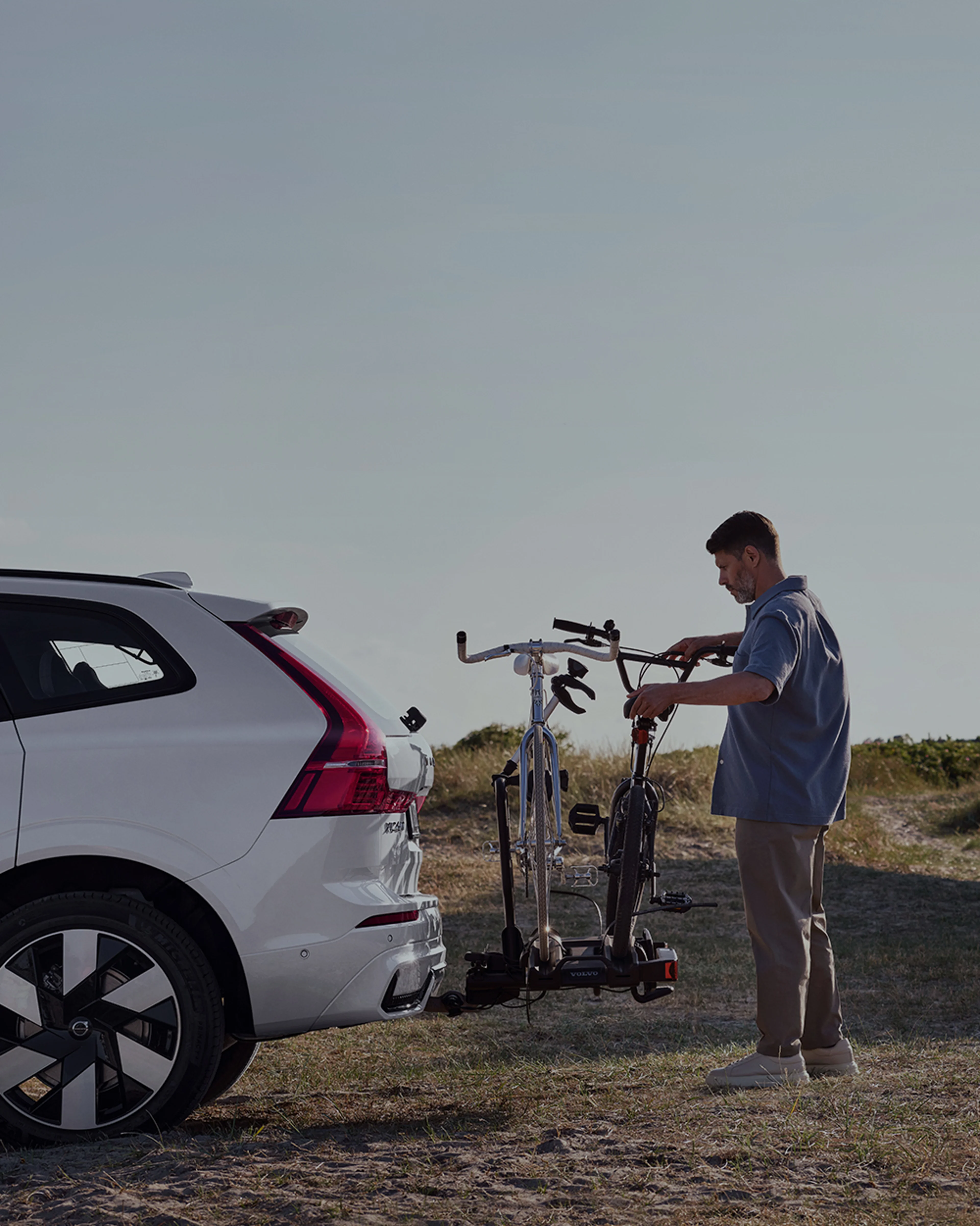 Un homme fixe des vélos sur un porte-vélos à l'arrière d'une Volvo XC60 blanche.