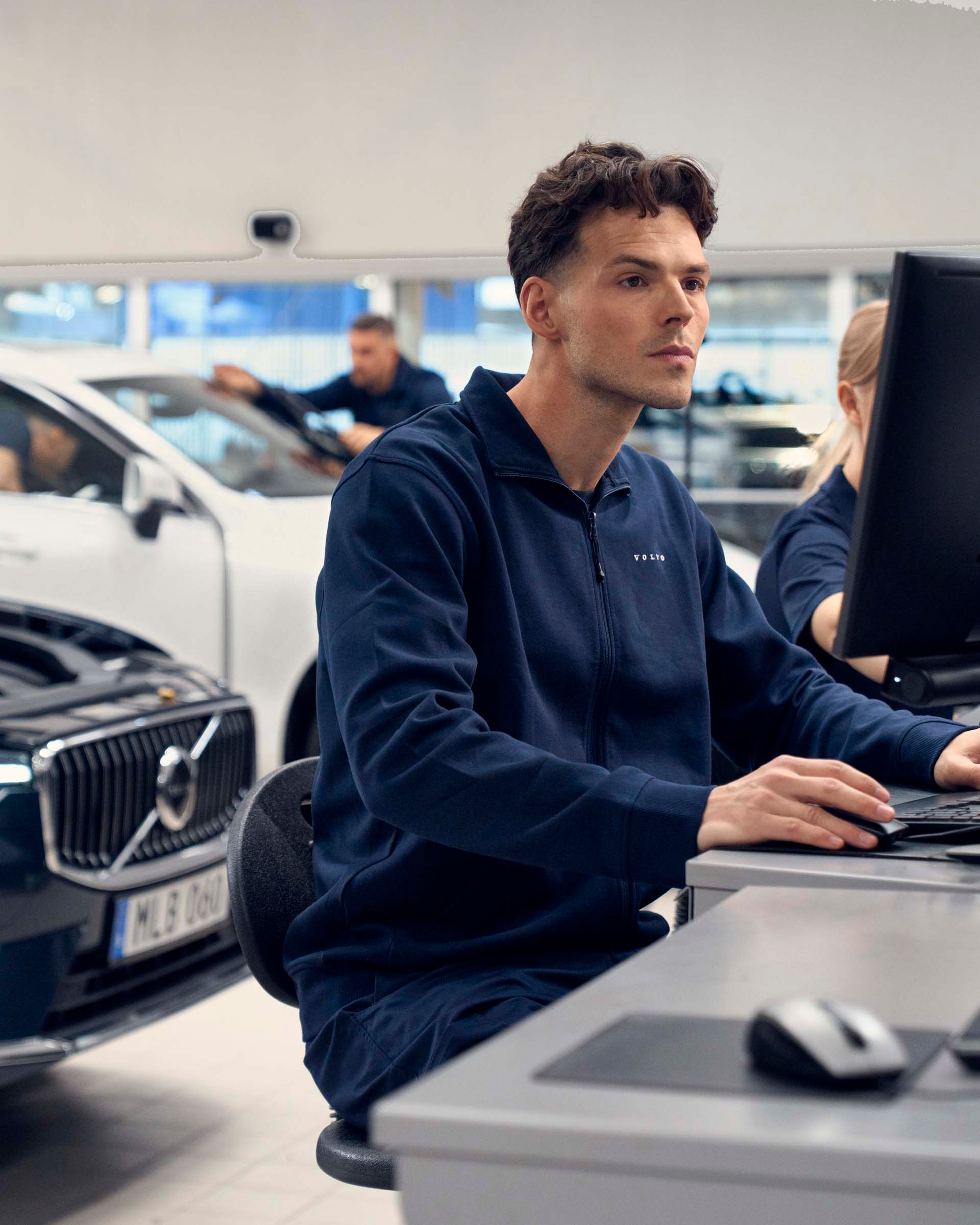 Un taller Volvo con mecánicos revisando coches y mirando datos en el ordenador sobre el vehículo