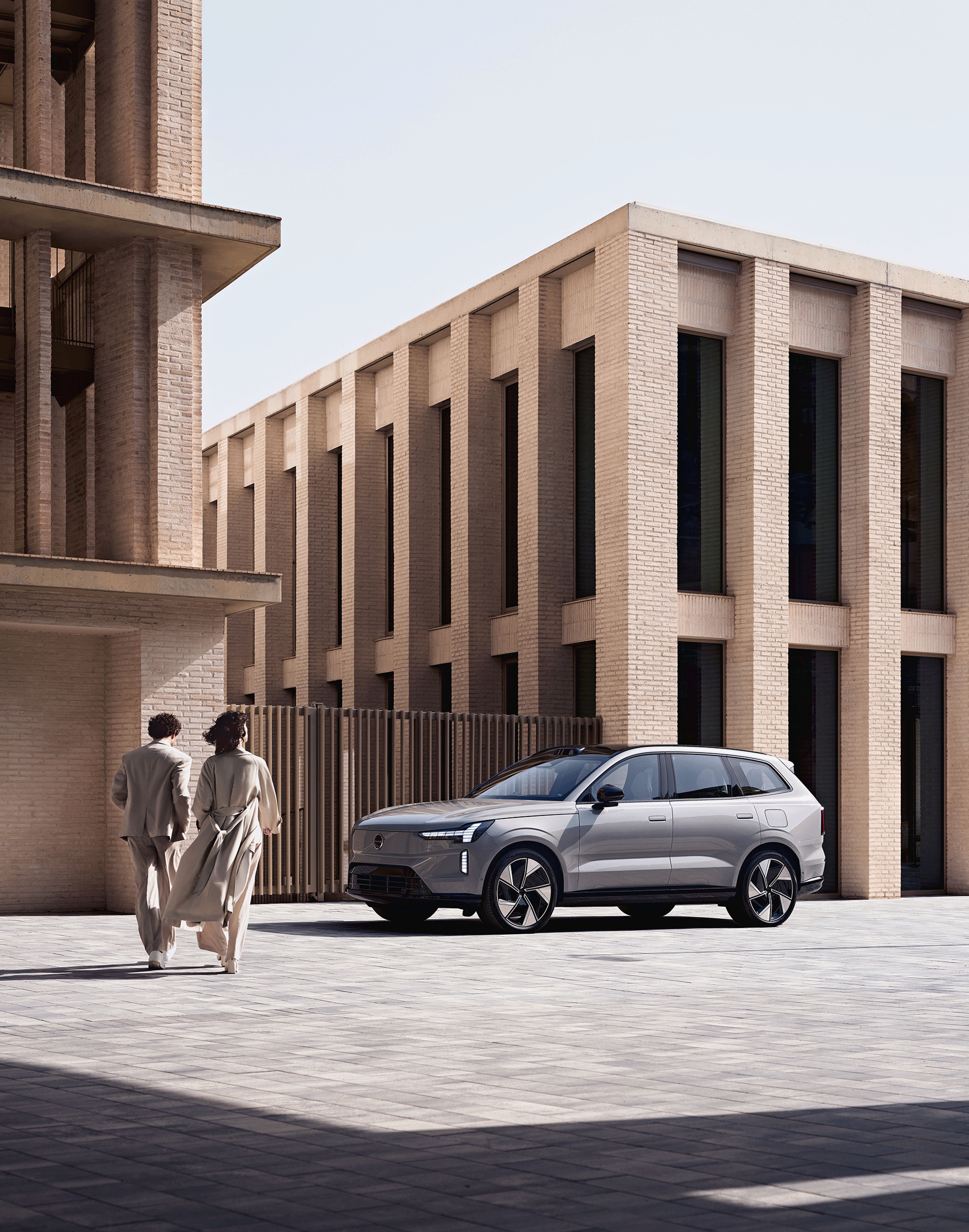 Zwei Personen laufen auf einen Volvo EX90 zu.