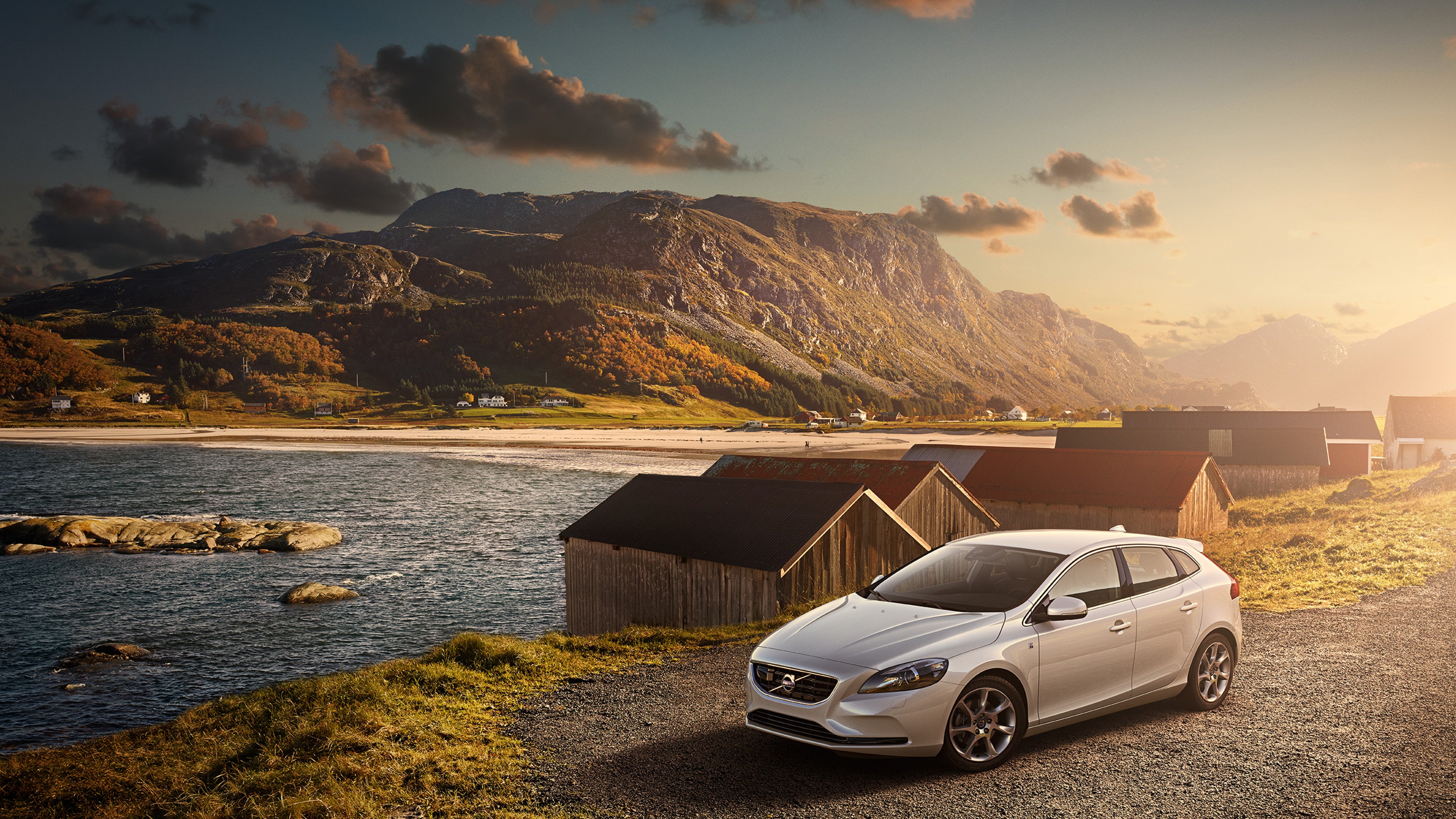 V40 cinzenta junto a uma paisagem montanhosa com cabanas e um lago no meio