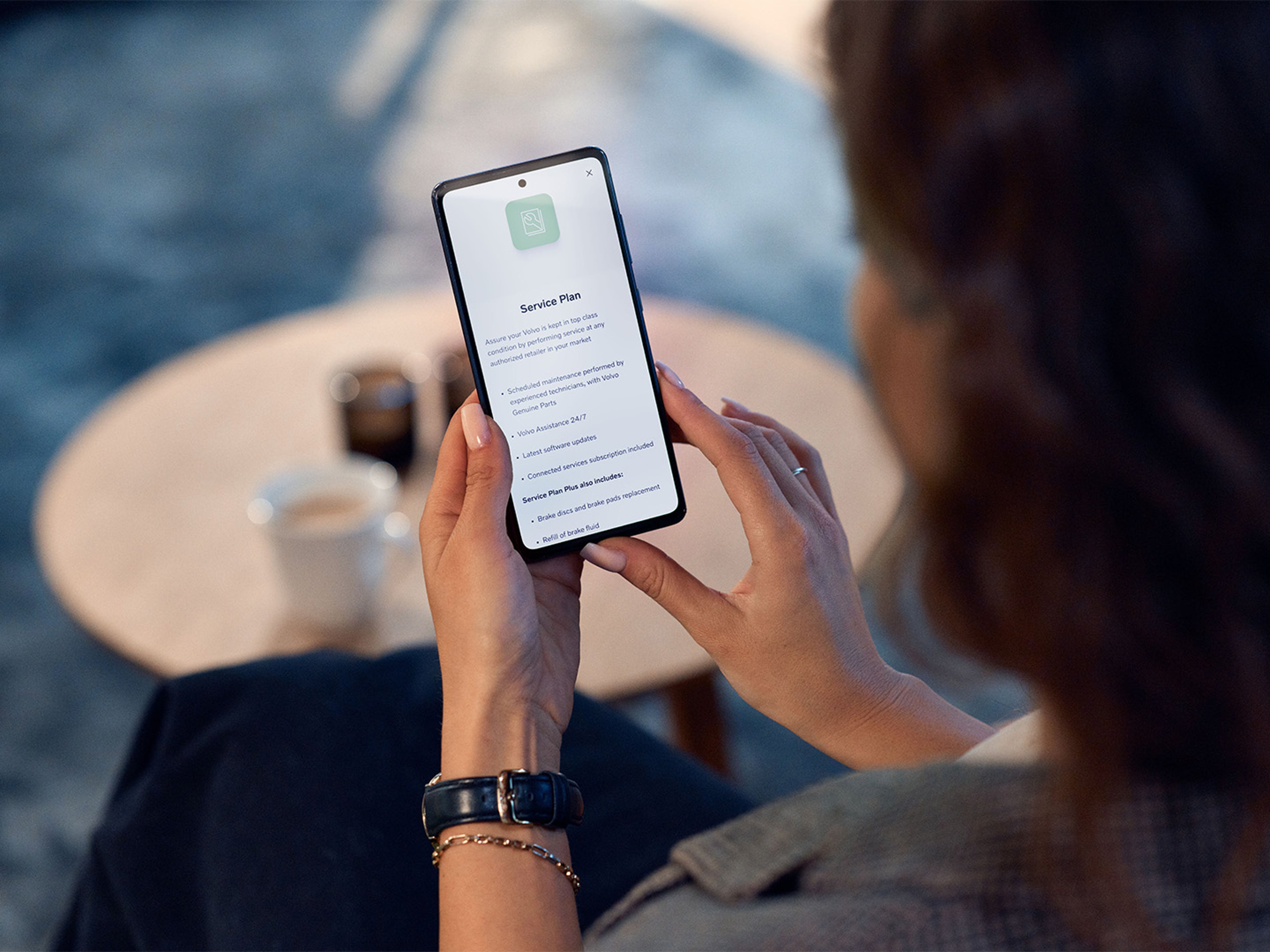 Imagem de um cliente segurando o seu telemóvel. O ecrã mostra os planos de assistência Volvo na aplicação Volvo Cars.