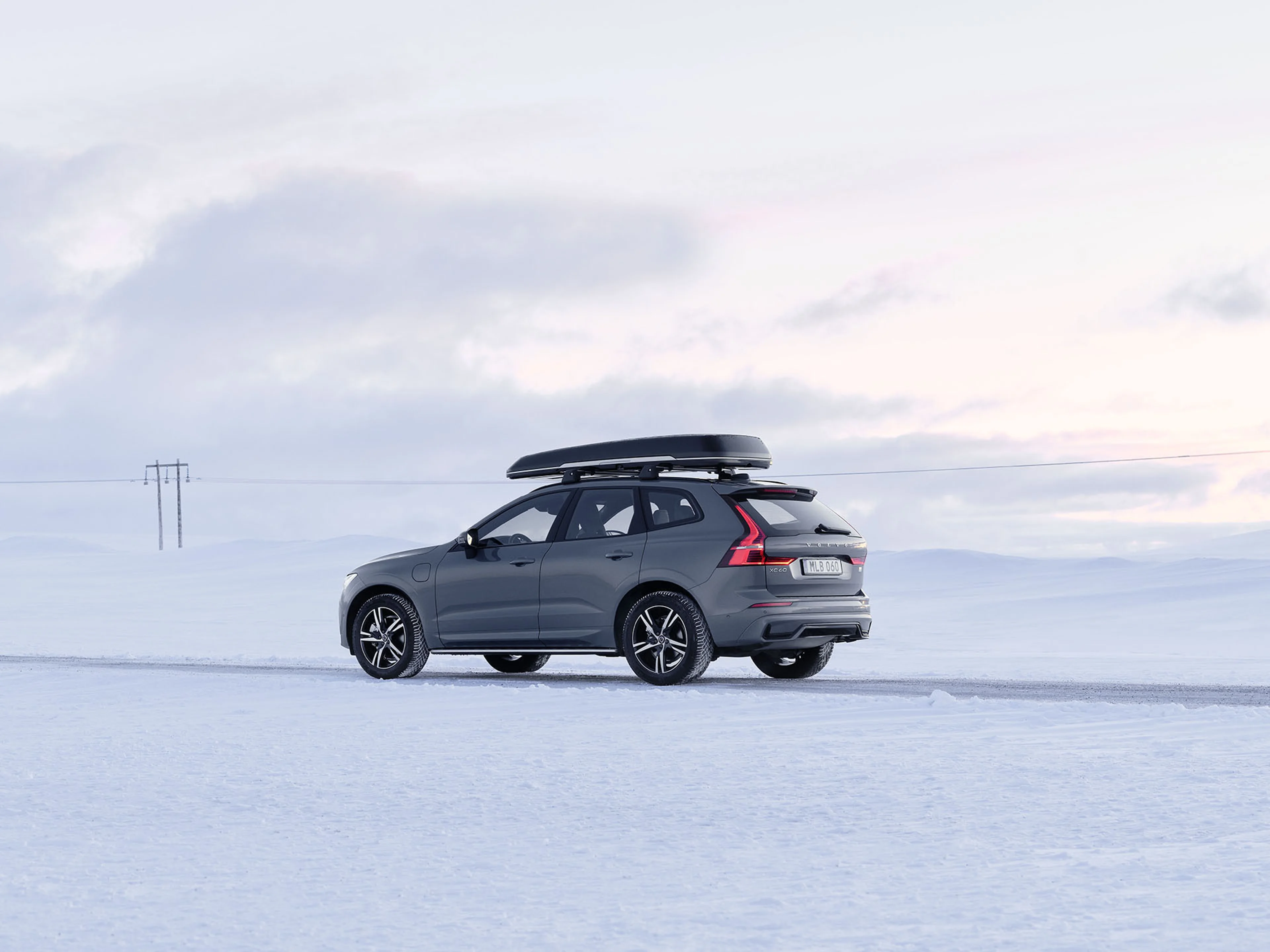 Volvo XC60 rijdend door sneeuwlandschap met dakkoffer en winterbanden