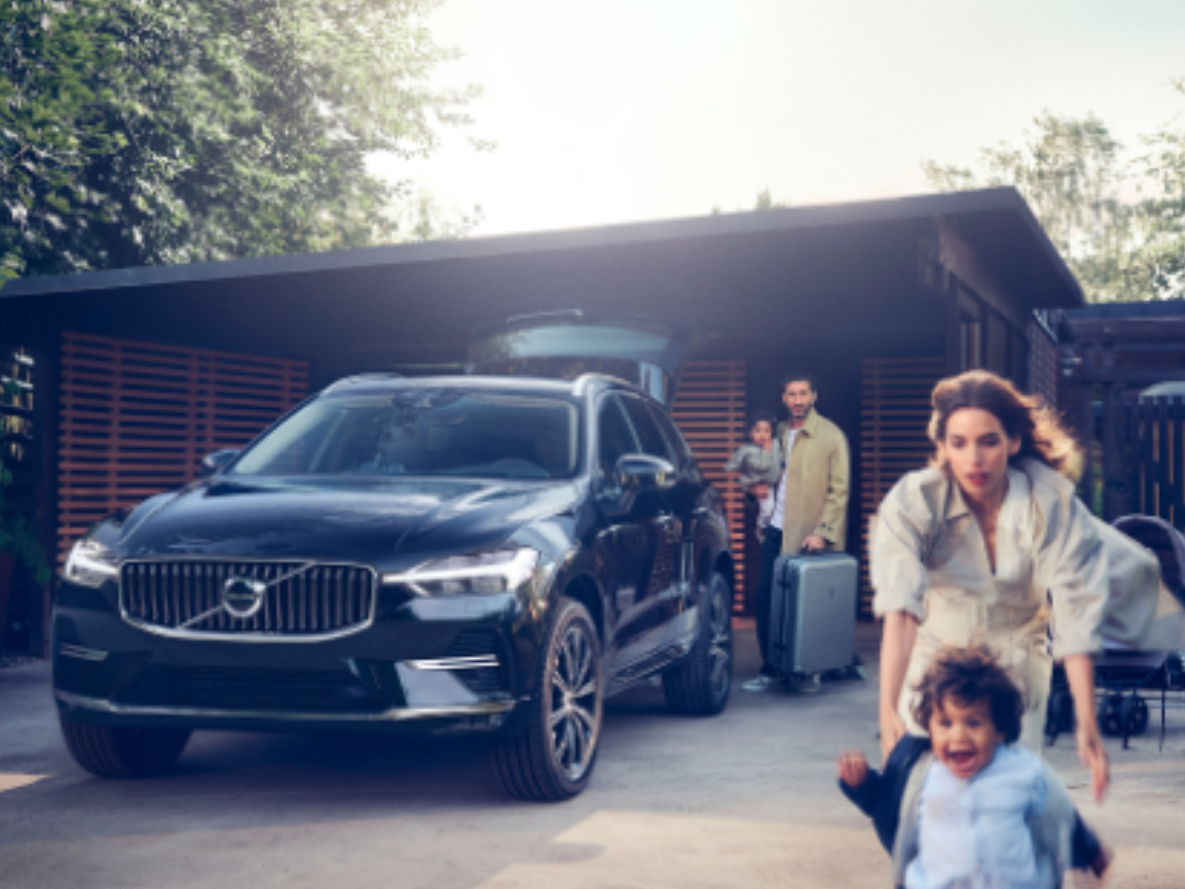 Eine Familie aus 4 Personen befinden sich um einen Volvo XC60 SUV, der sich vor einem Haus befindet.