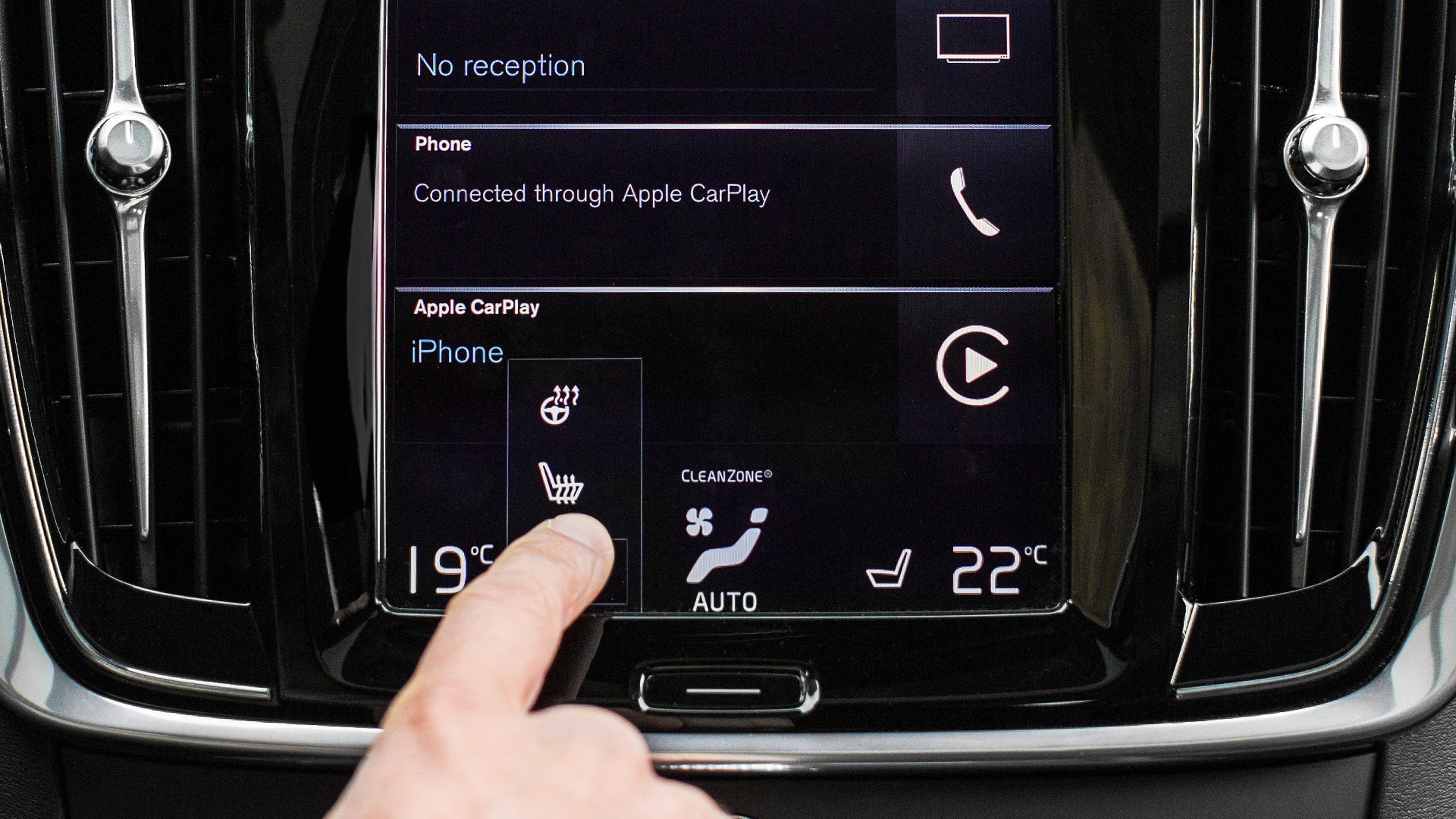 Boardcomputer mit einem Finger der auf die Sitzheizungstaste zeigt.