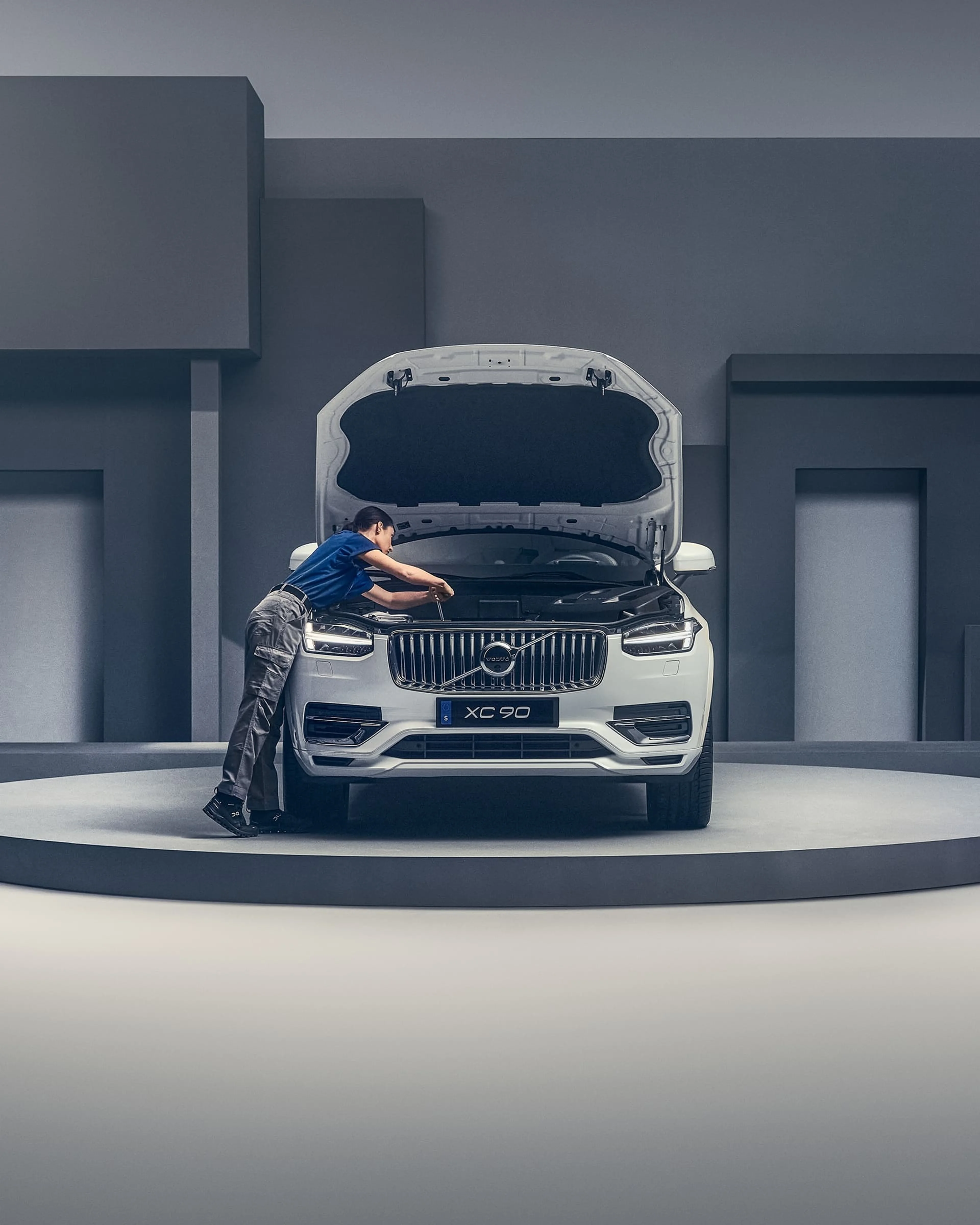 Un mécanicien travaille sur le moteur ouvert d'une Volvo XC90 blanche dans un atelier.