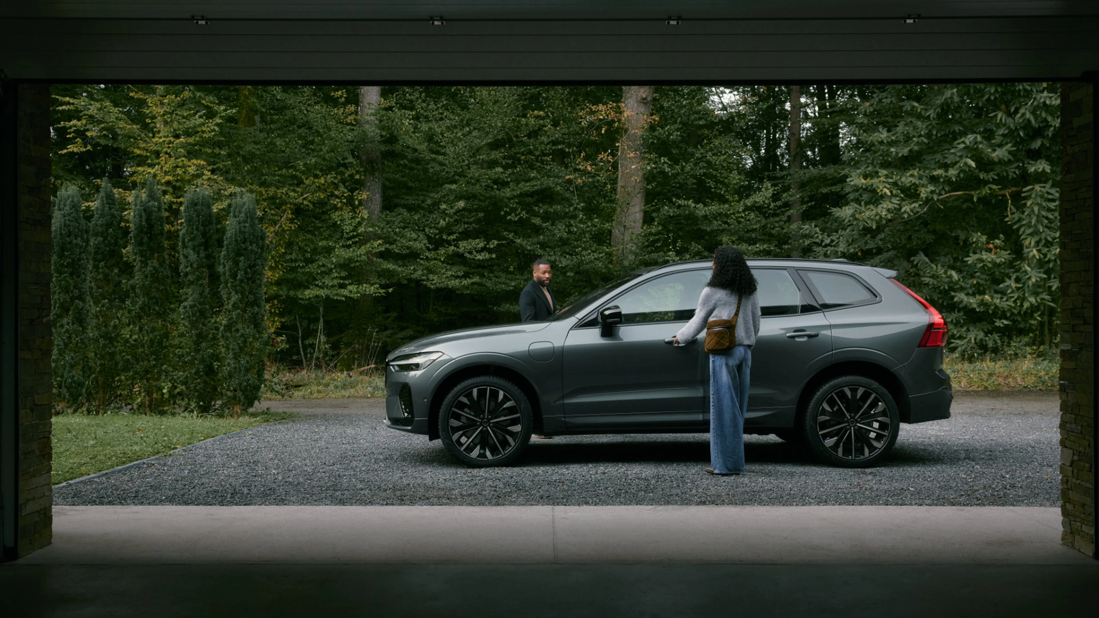 Ein Volvo XC60 Plug-in Hybrid in der Farbe Forest Lake vor einem See im Wald