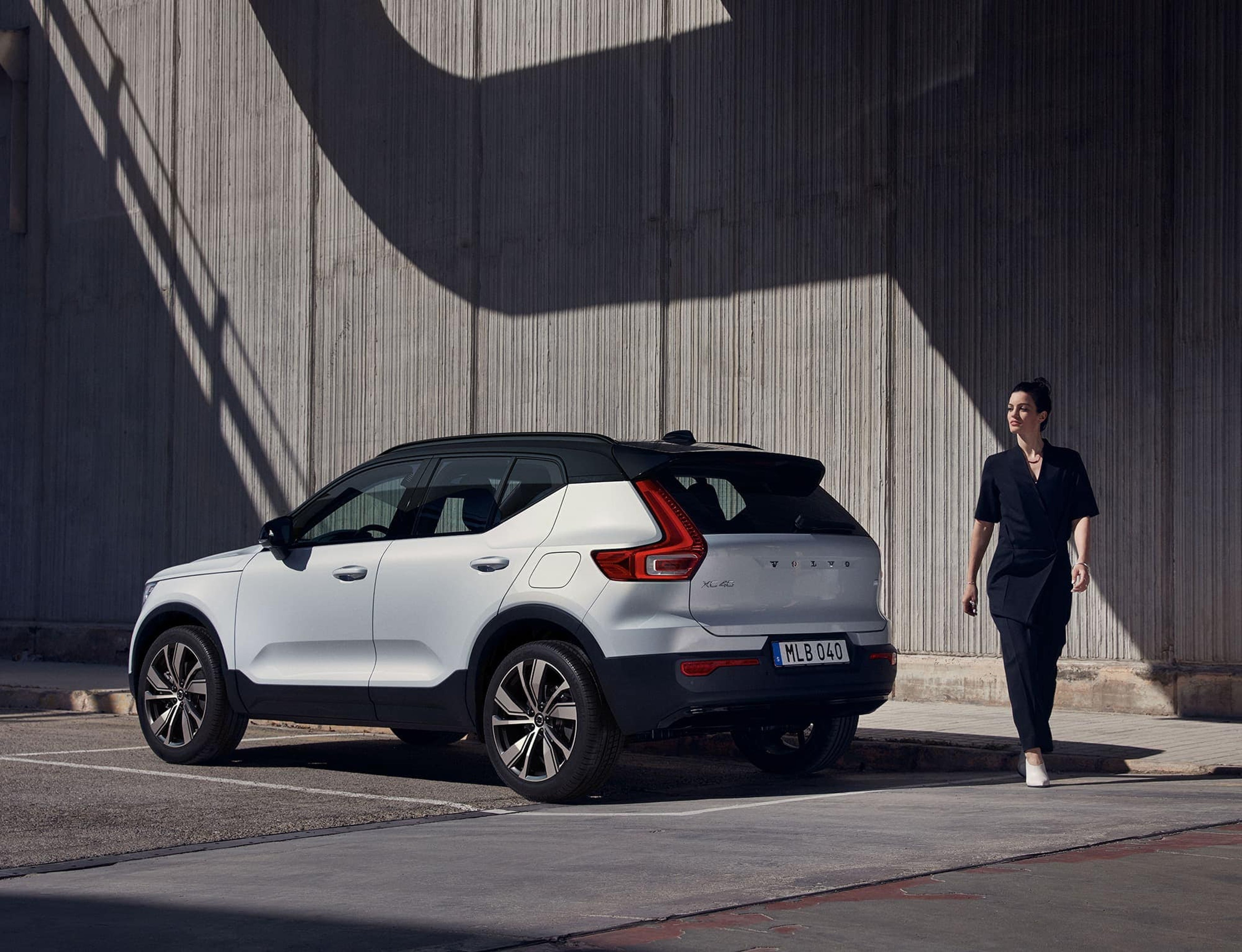 Witte Volvo XC40 tegen een betonnen muur, met een vrouw die langs de achterkant kruist.