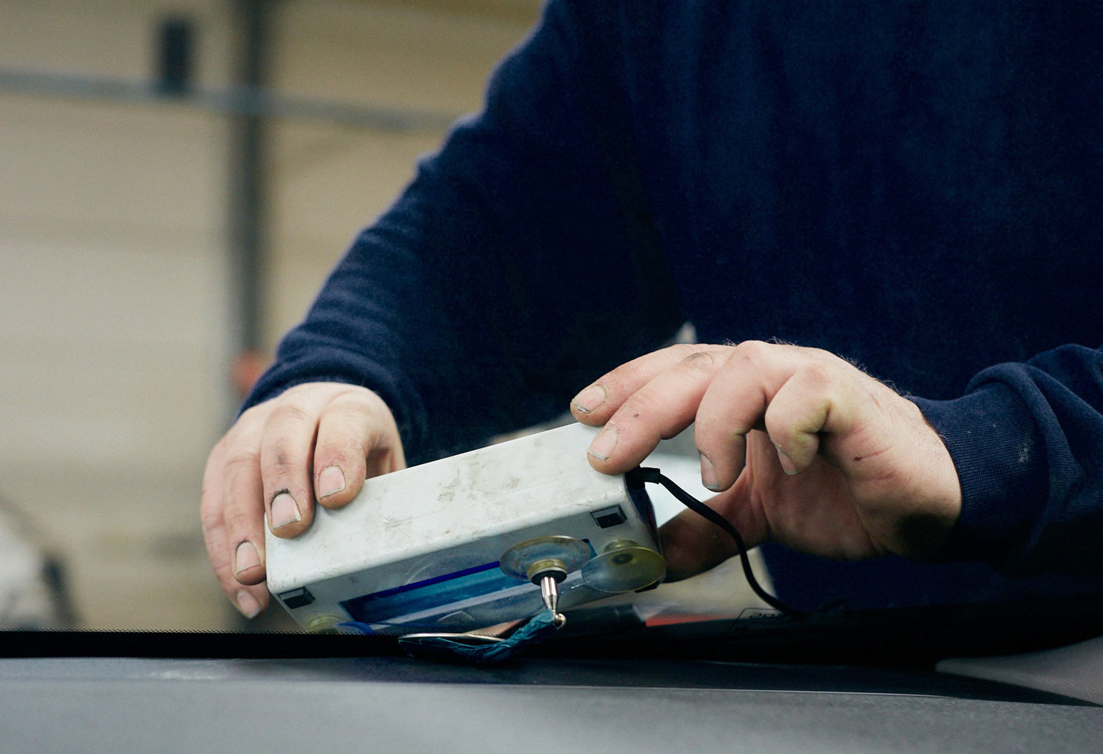 Gros plan d'un technicien qui répare un impact sur le pare-brise d'une Volvo avec un outil spécial.
