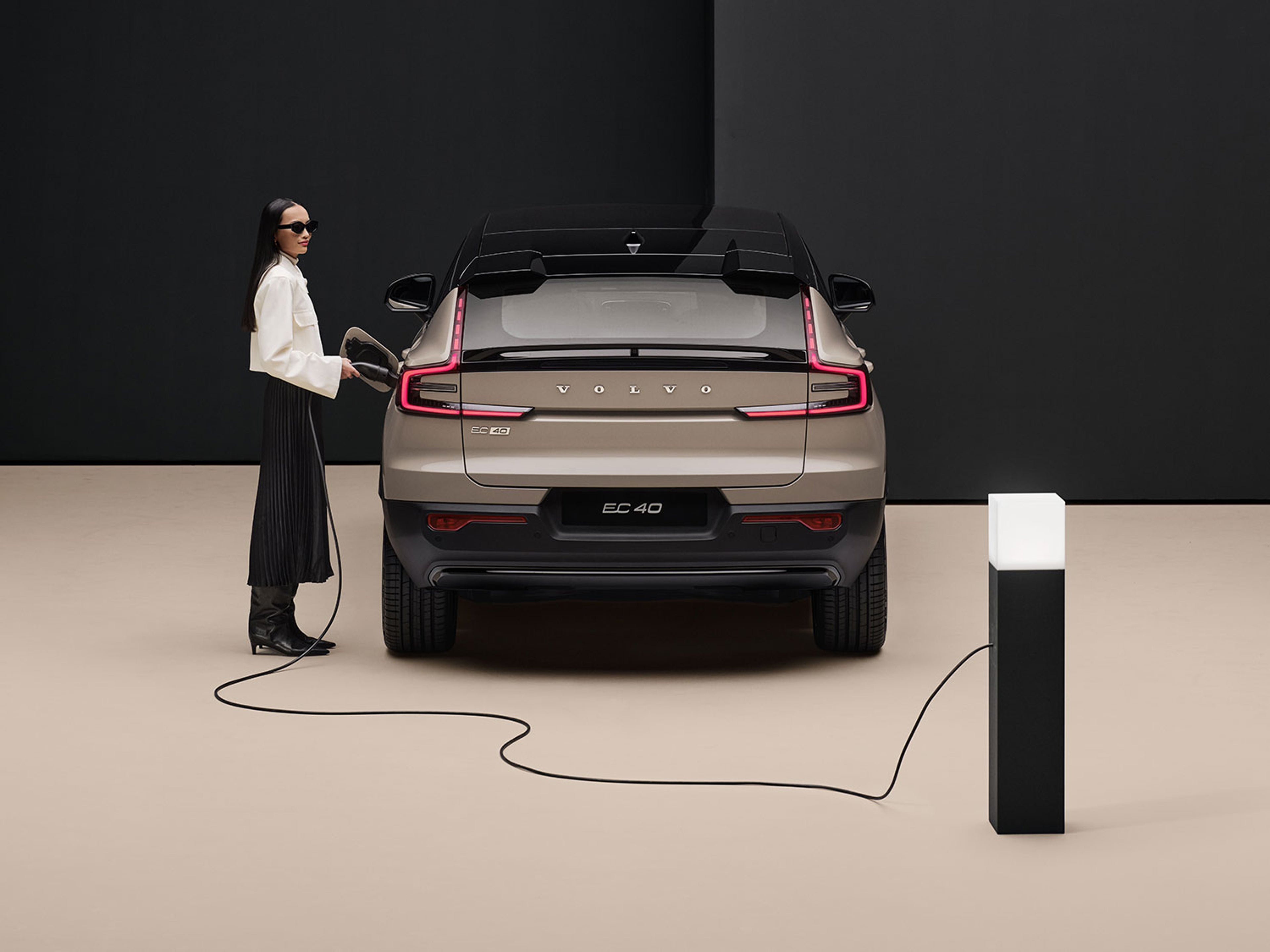 Arrière d’un Volvo XC40 électrique avec une personne tenant un câble de recharge branché à une borne