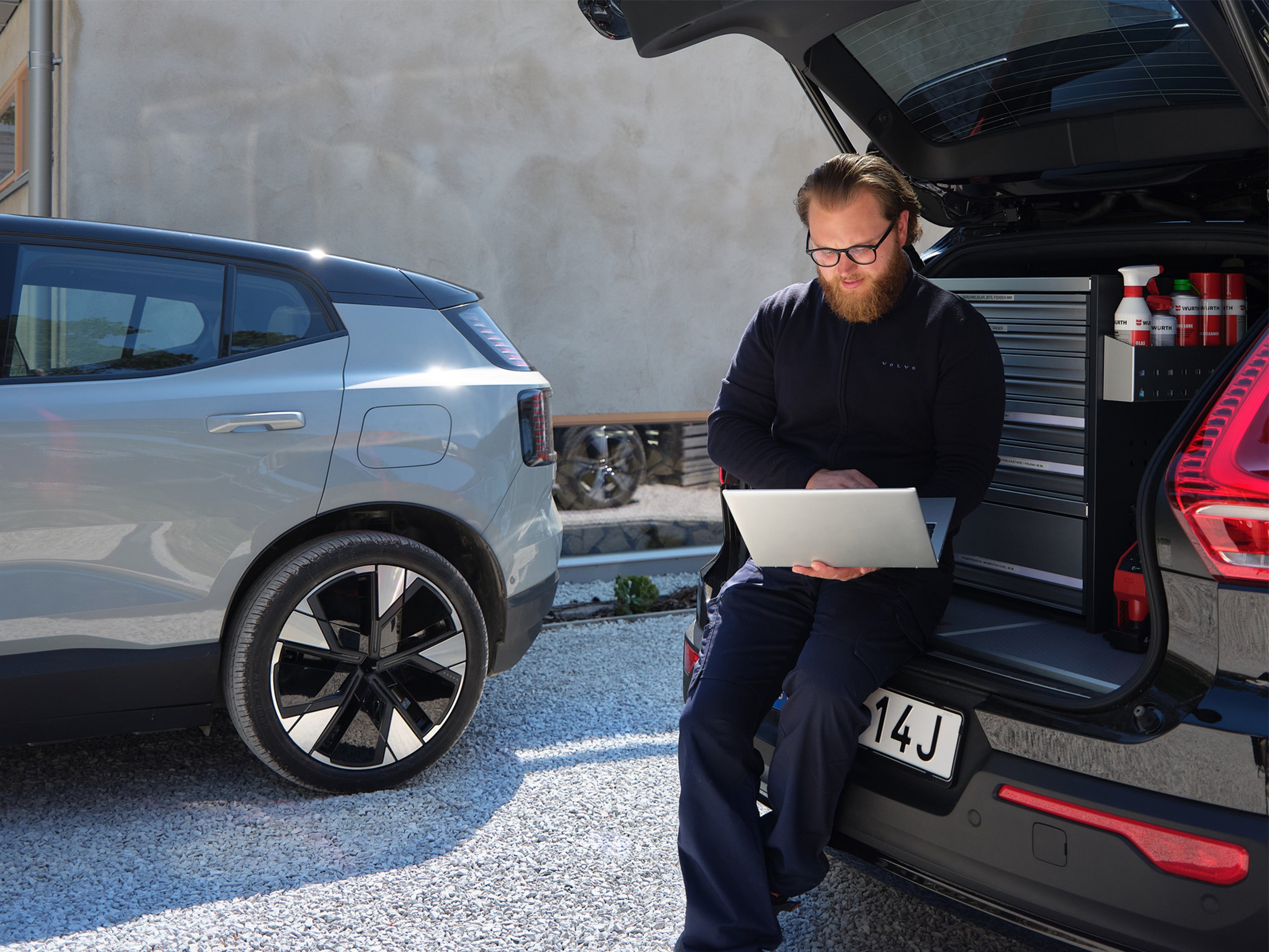 Volvo Mobile Service mekaanikko istuu huoltoauton avoimen takatilan reunalla ja tutkii tietokonettaan.