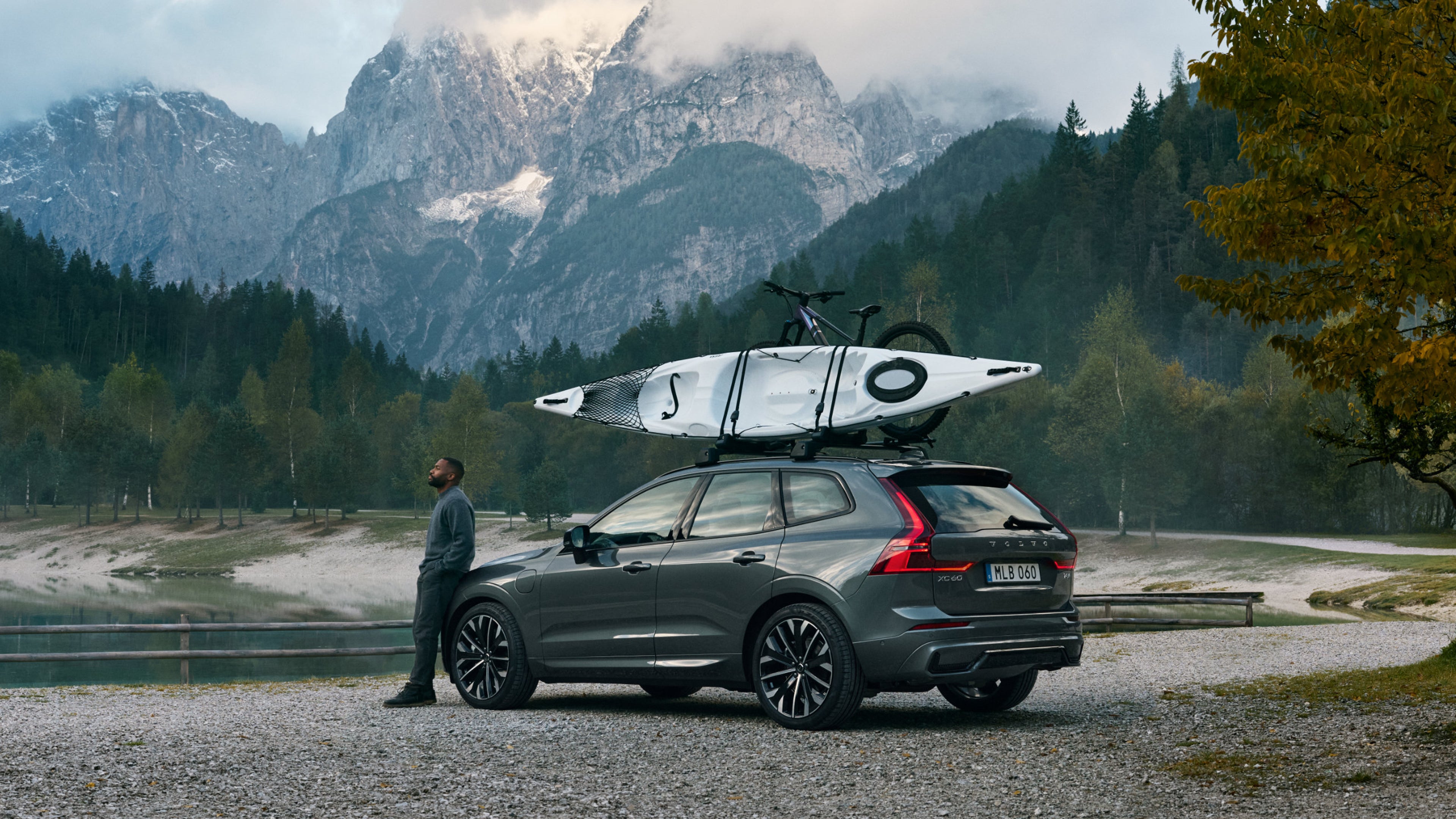 Ein Mann steht an einem dunkelgrauen Volvo XC60 SUV gelehnt und schaut in den Himmel.