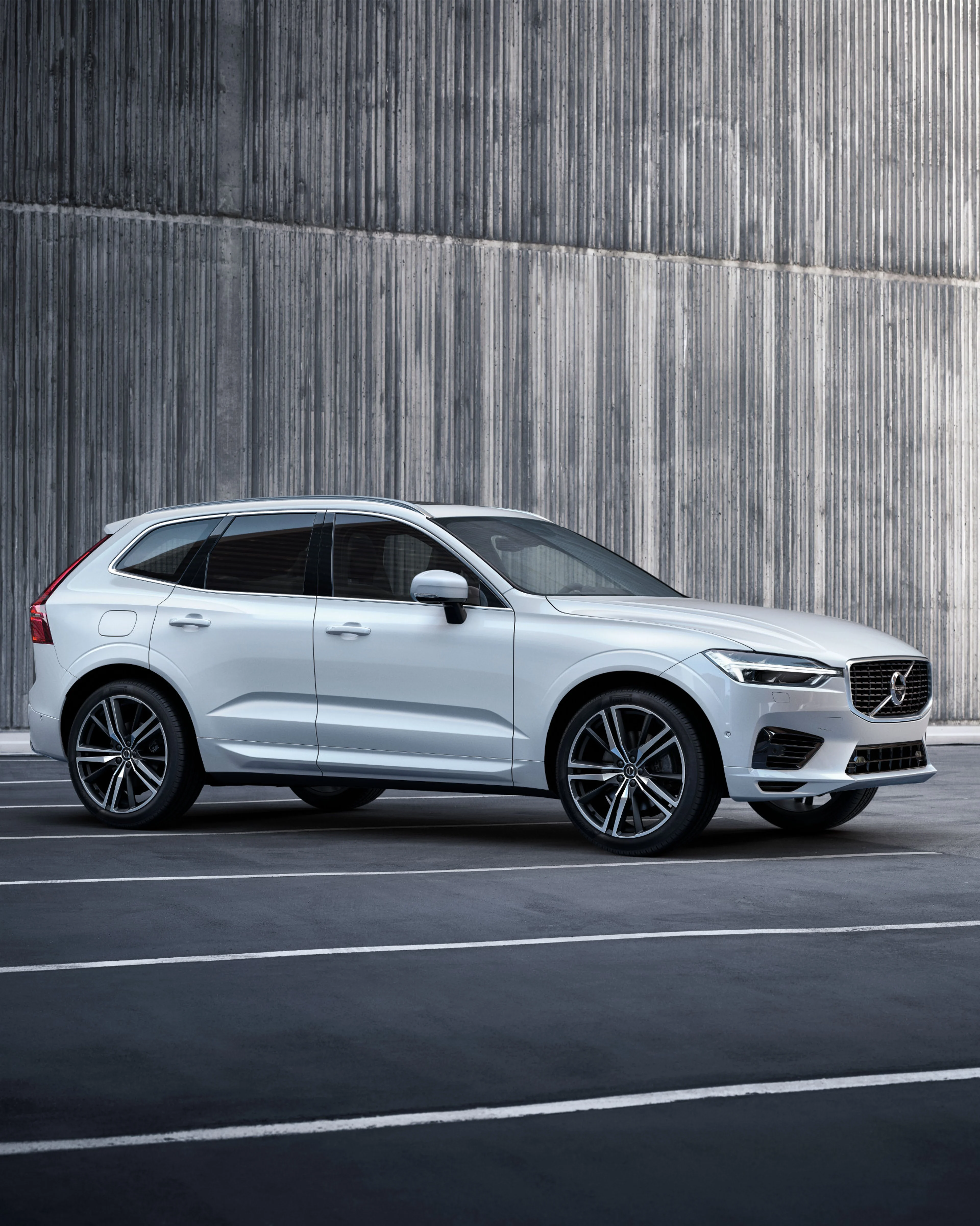 Ein Volvo XC60 in Silver Dawn steht seitlich auf einem Pakrplatz vor einer grau-mellierten Wand.