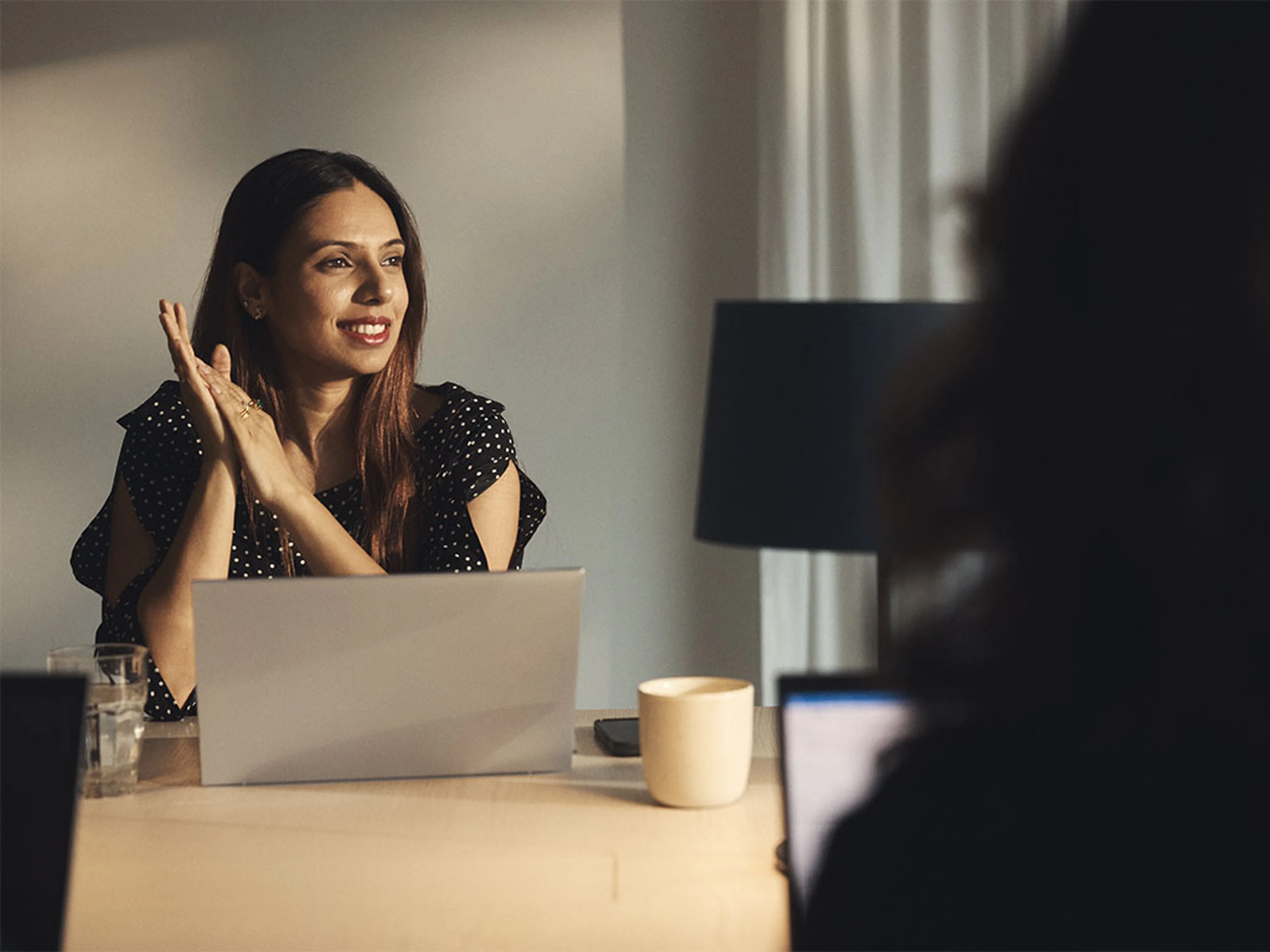 Femme devant un ordinateur portable sur une table, une personne floue au premier plan.