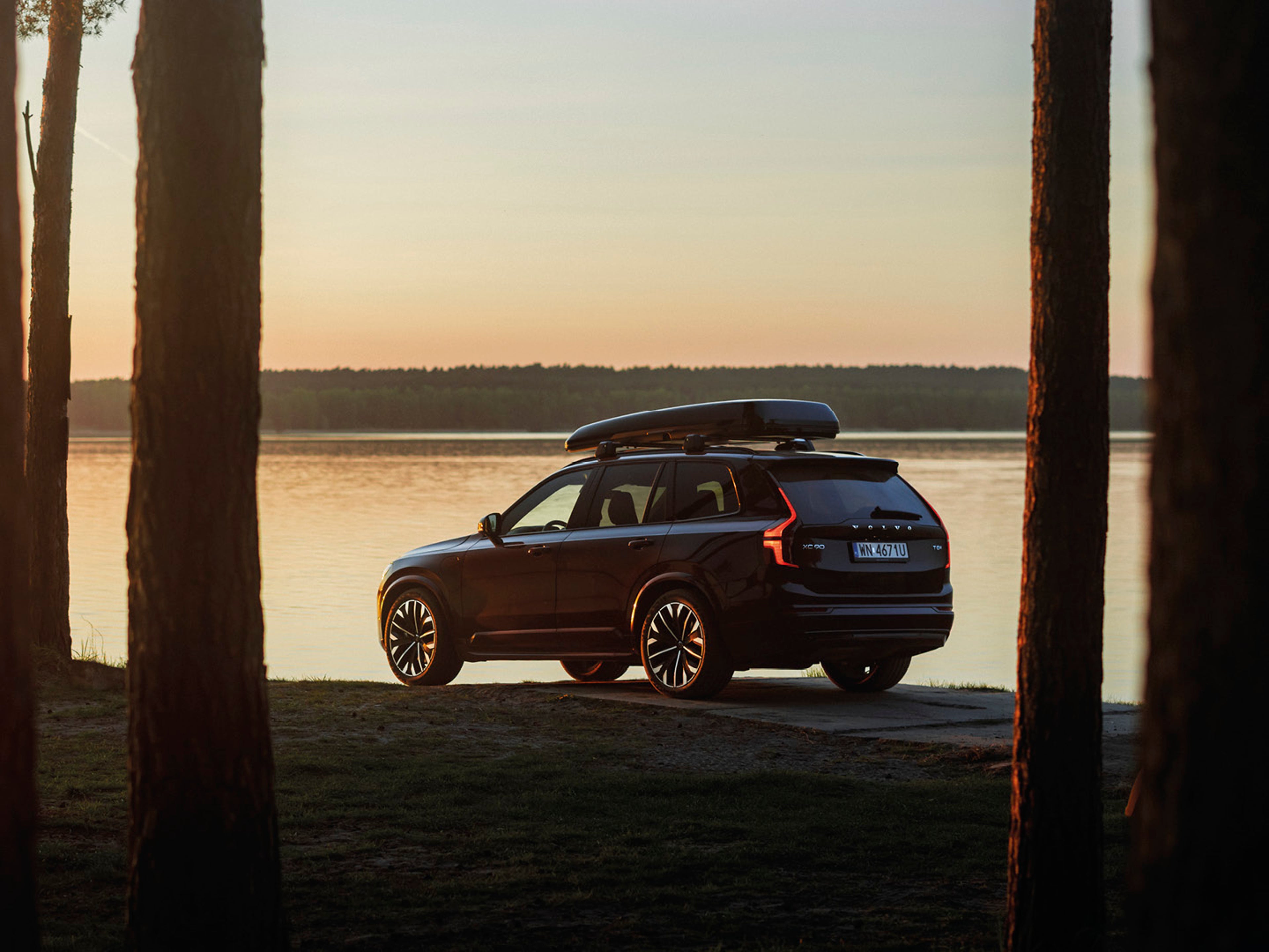 Volvo XC90 nad brzegiem jeziora pośród drzew