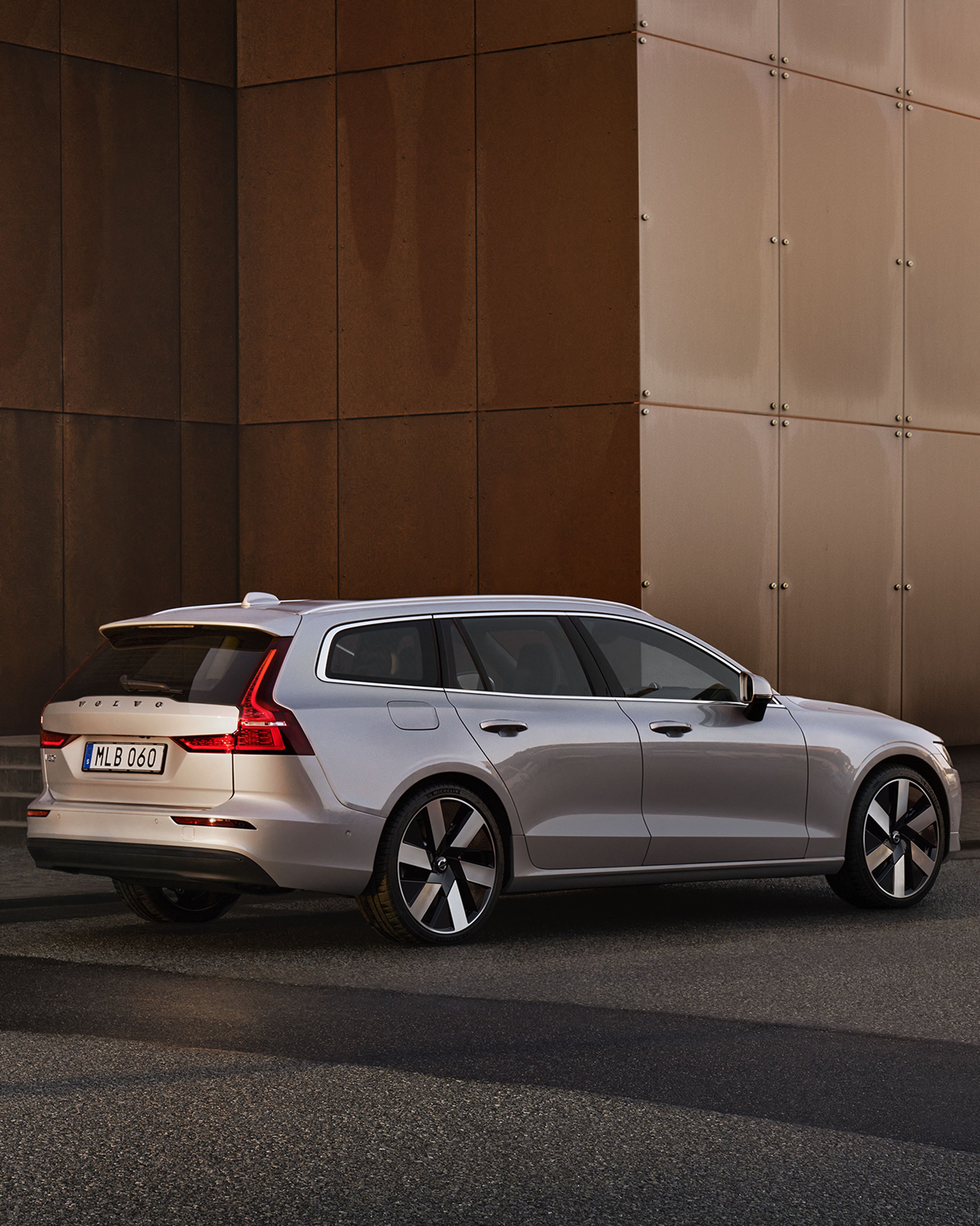 Der Volvo V60 steht vor einer braunen Wand draußen. Draufsicht auf das seitliche Heck des Fahrzeugs in silber.