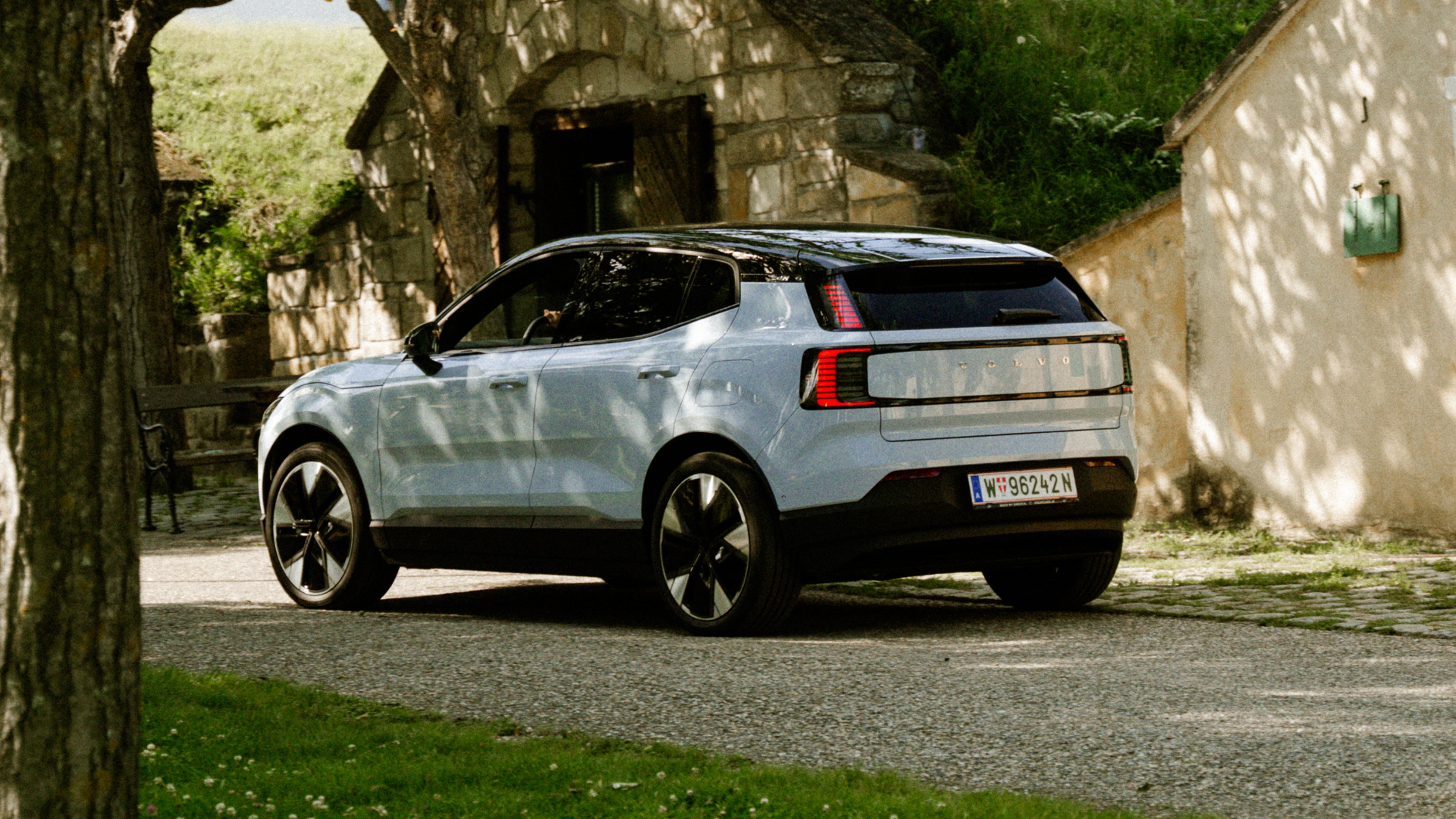 Ein weißer Volvo EX30 steht in der Natur zwischen Häusern, deren Dächer mit Gras bedenkt sind.