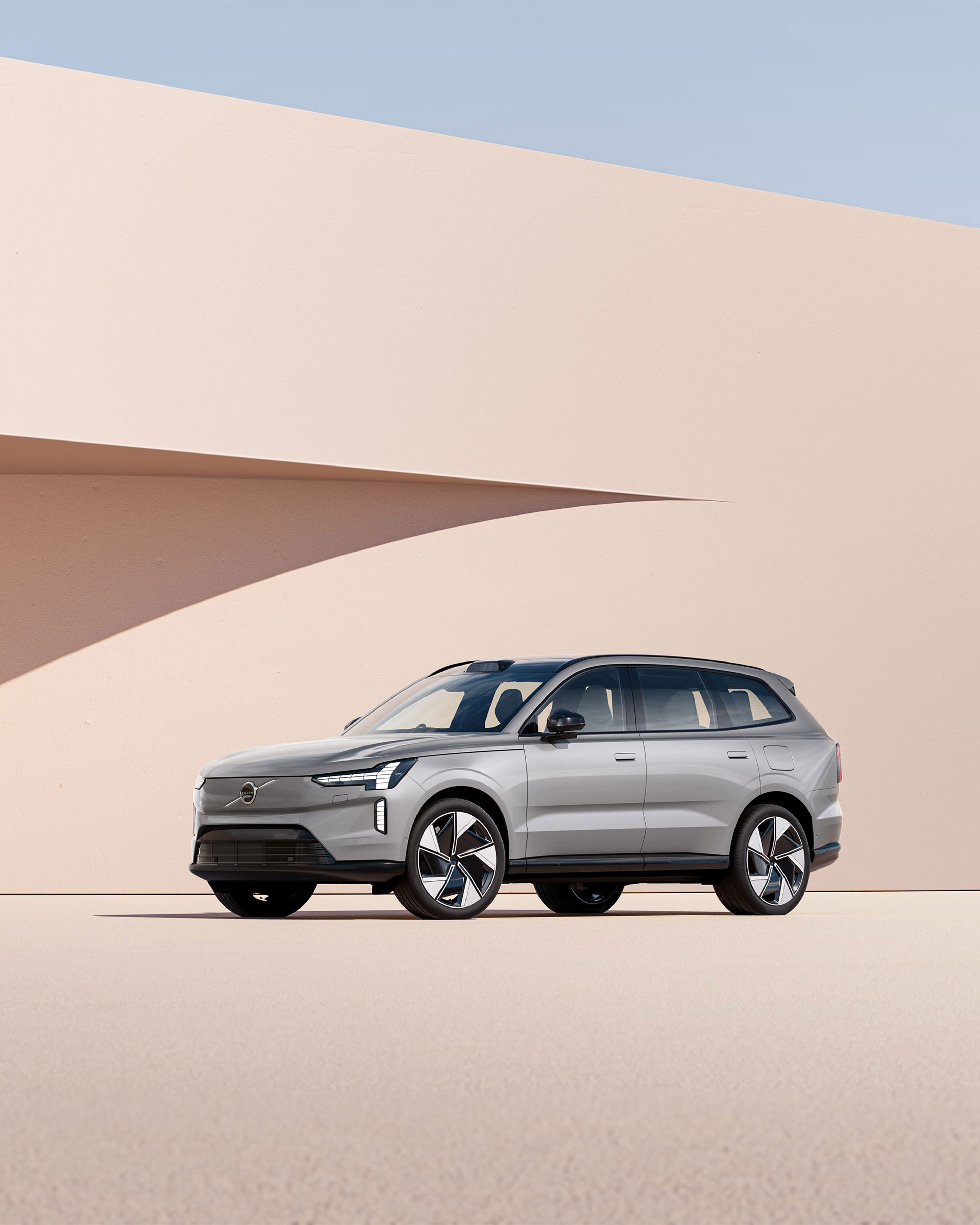 Volvo EX90 argenté garé devant un mur beige avec une ombre projetée