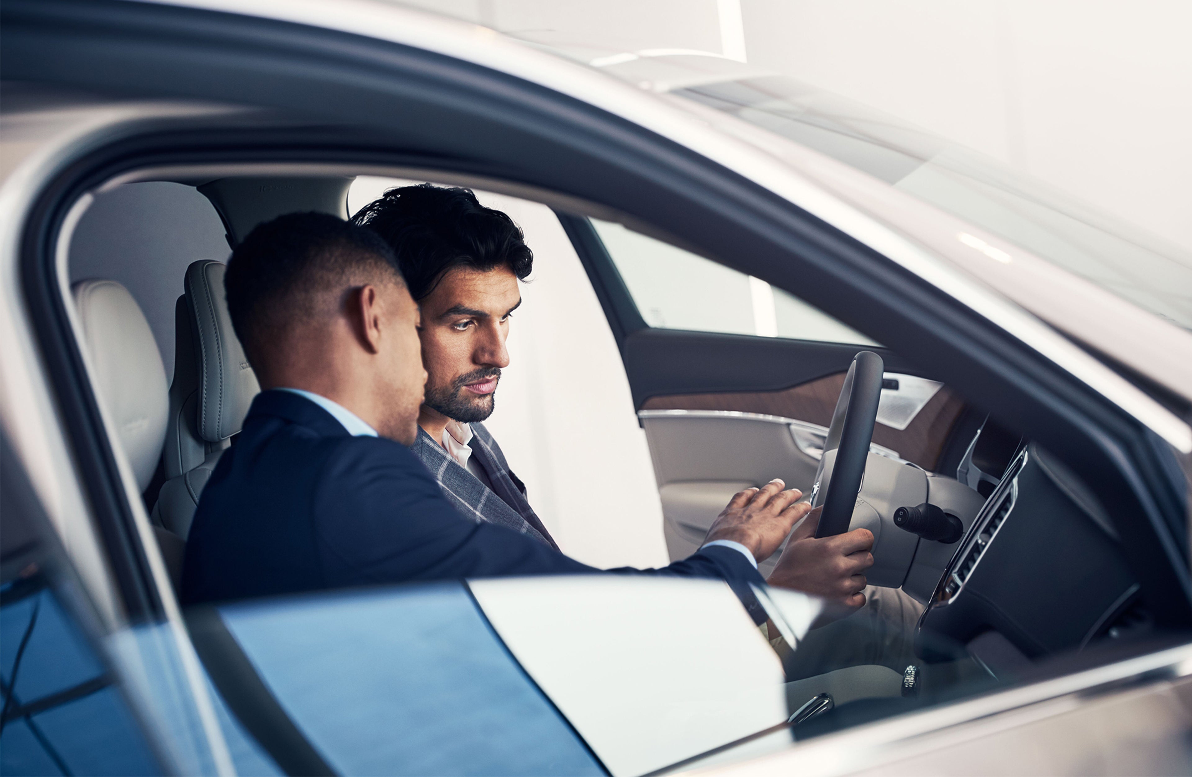 To personer sitter i en bil og ser på rattet, sett fra siden