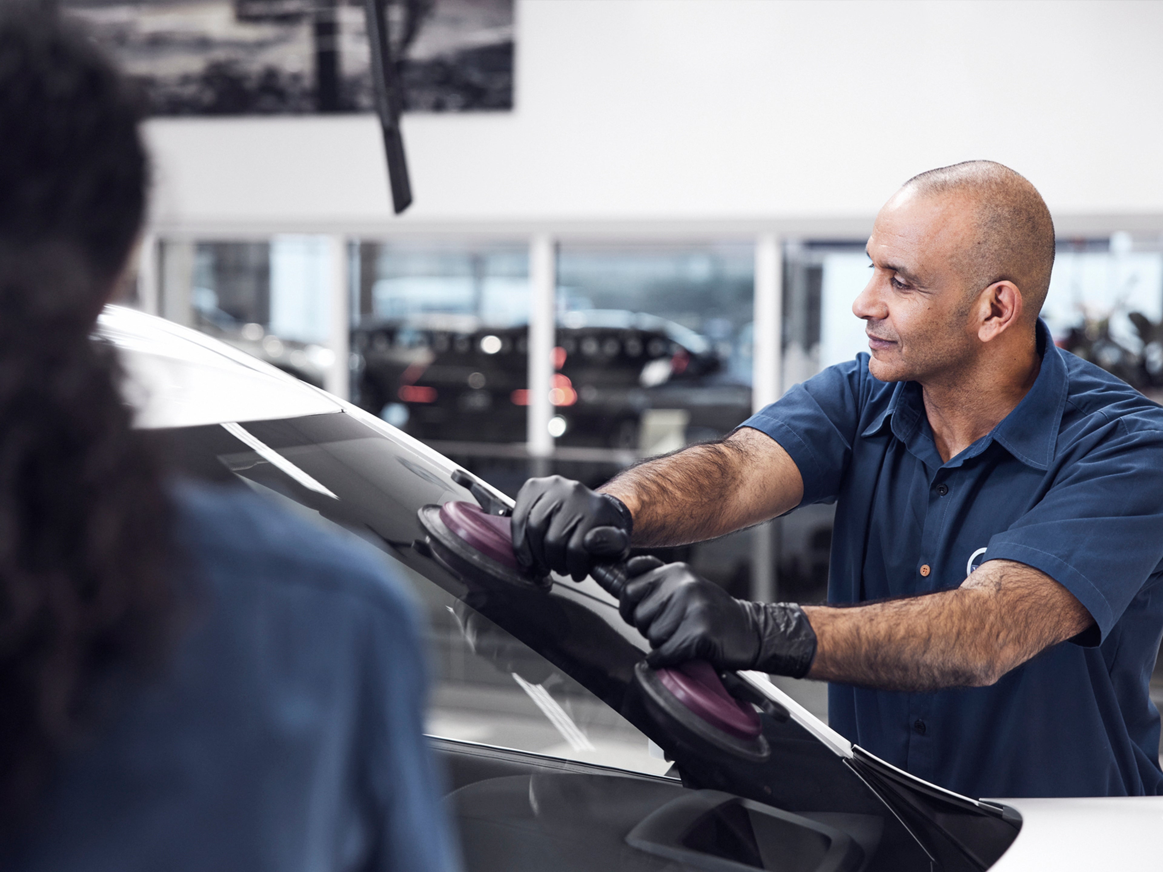 Un técnico de servicio dando mantenimiento al parabrisas de un vehículo.