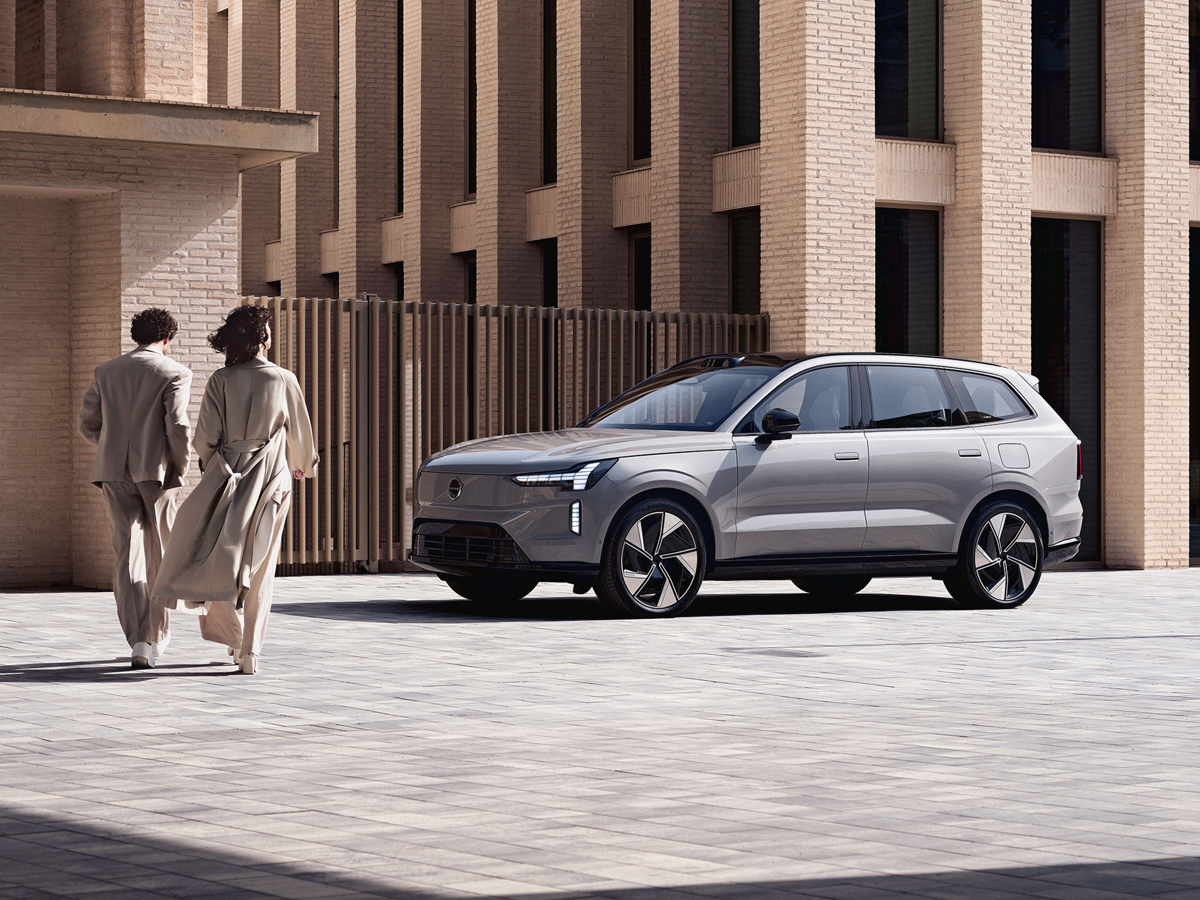 Zwei Personen laufen auf einen Volvo EX90 zu.