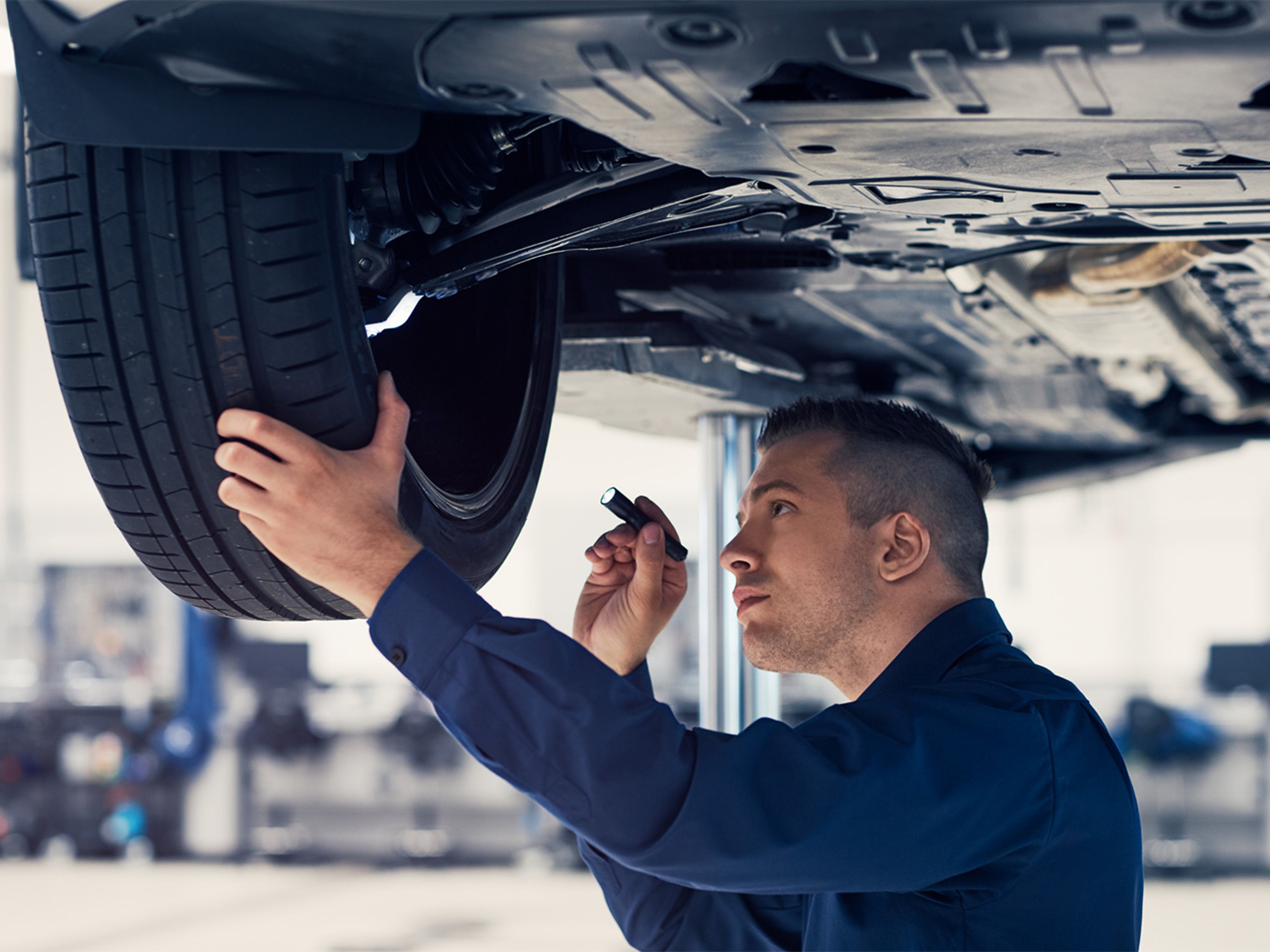 Volvo expert examining underside of a car and shining a torch at the tyre