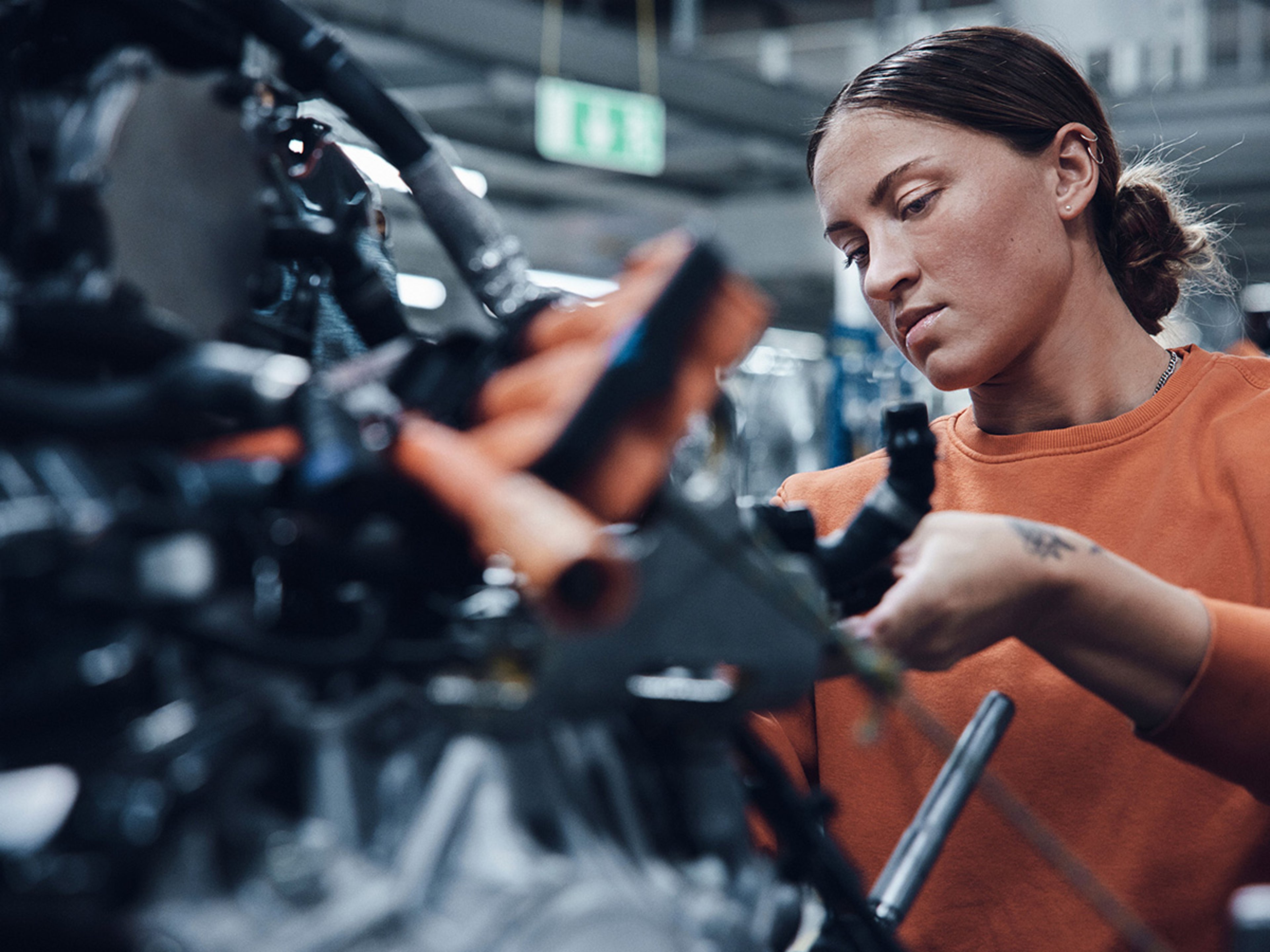 Een vrouw met een oranje trui werkt geconcentreerd aan een motor in een Volvo-werkplaats.