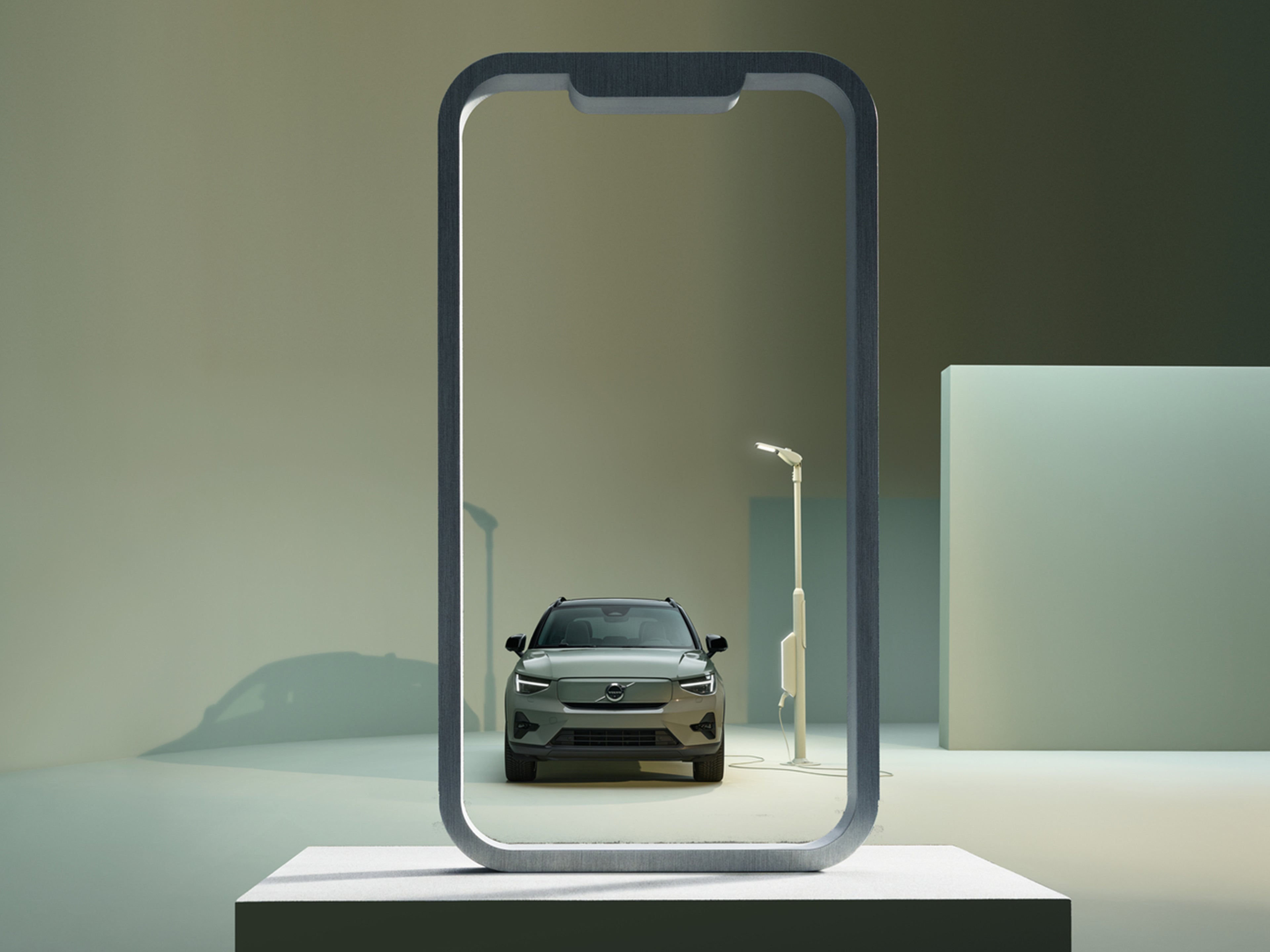 Lataukseen kytketty Sage Green -värinen Volvo EX40 auto puhelimen ruudun kehystämänä.