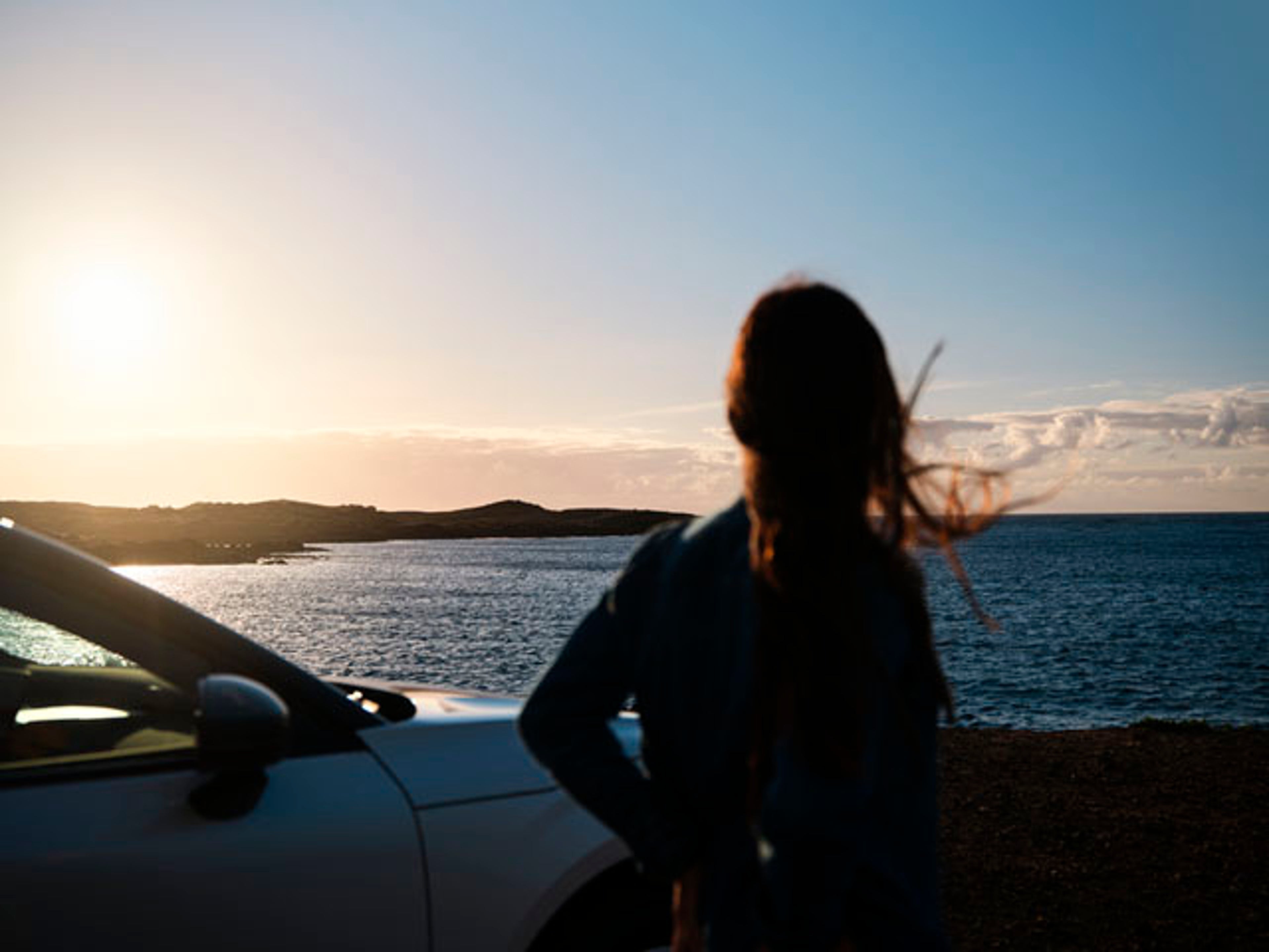 Una chica mirando el horizonte al lado de un vehículo volvo