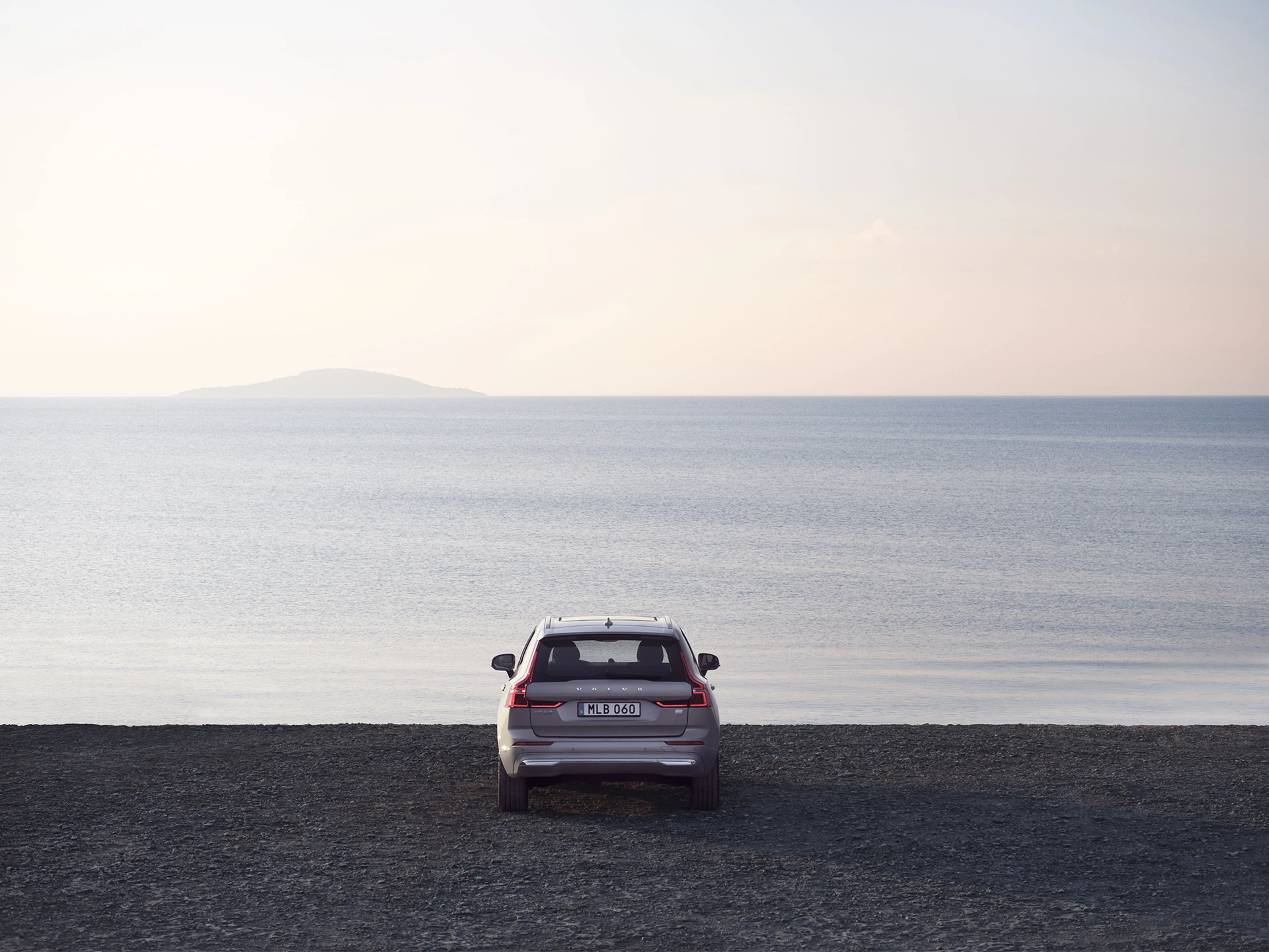 Ein anthrazitfarbener Volvo XC60 in Heckansicht steht mit der Front zum Meer gerichtet auf einem Strand aus Geröll.