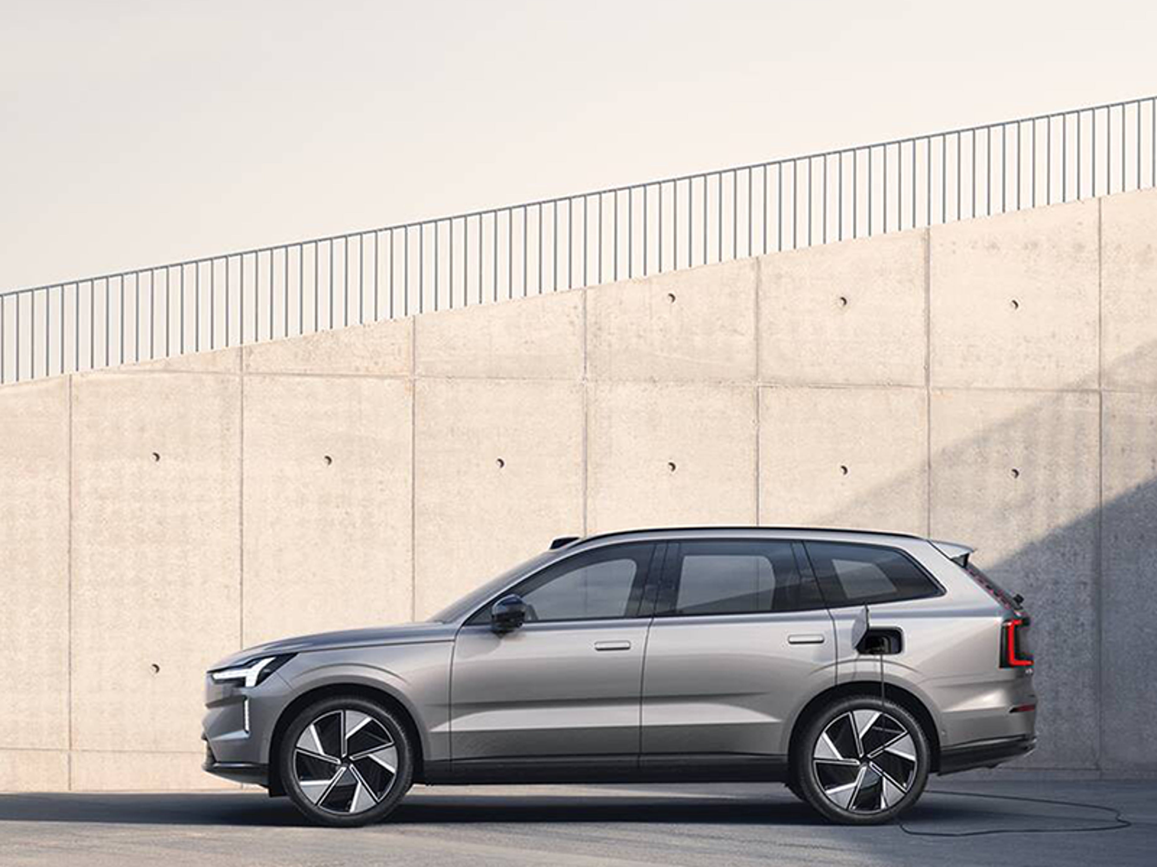 En elegant, moderne Volvo SUV med blank finish er parkeret på en solrig, tom plads. SUV’ens design er kantet og futuristisk og udstråler innovation.