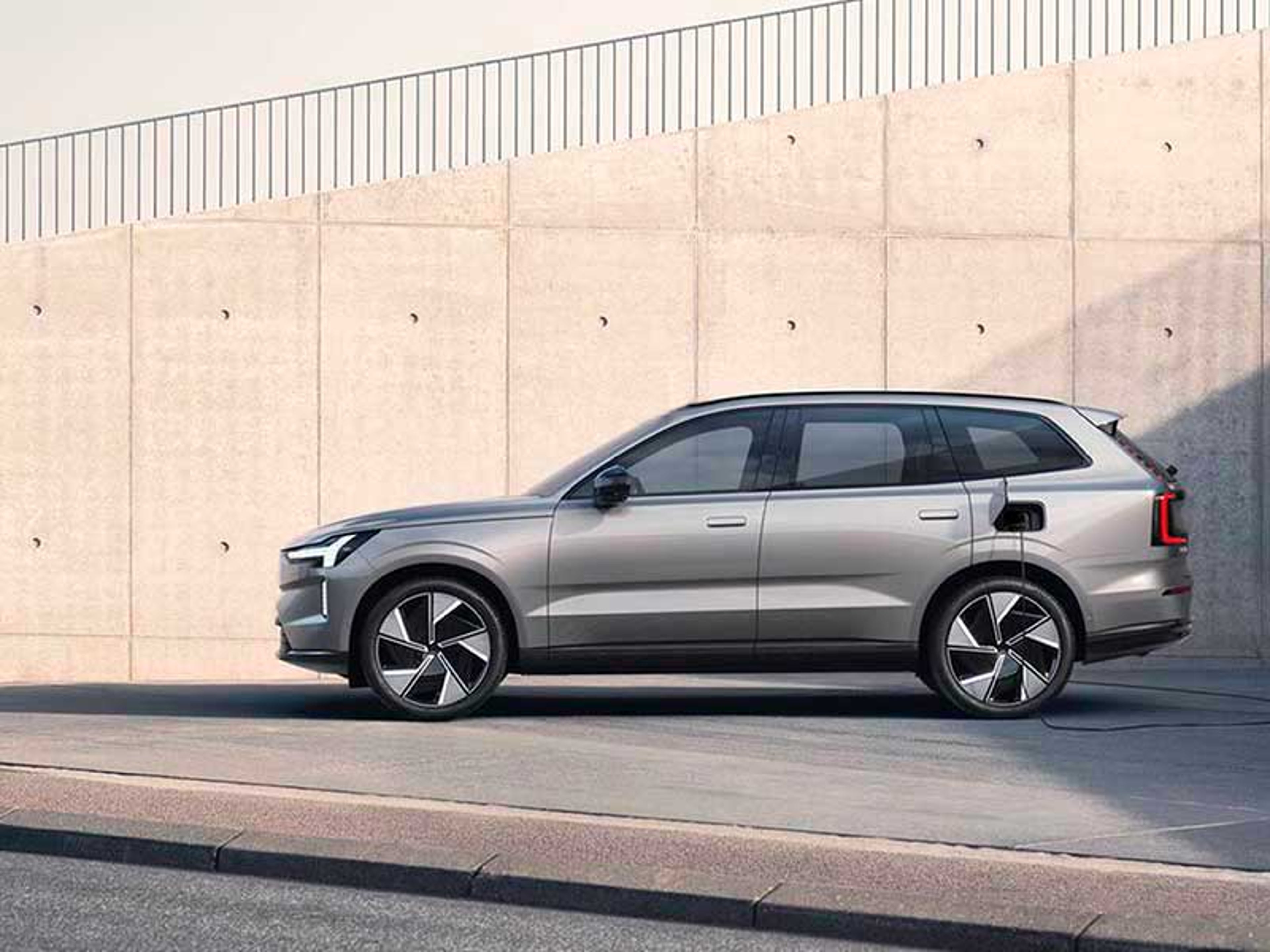 En elegant, moderne Volvo SUV med blank finish er parkeret på en solrig, tom plads. SUV’ens design er kantet og futuristisk og udstråler innovation.