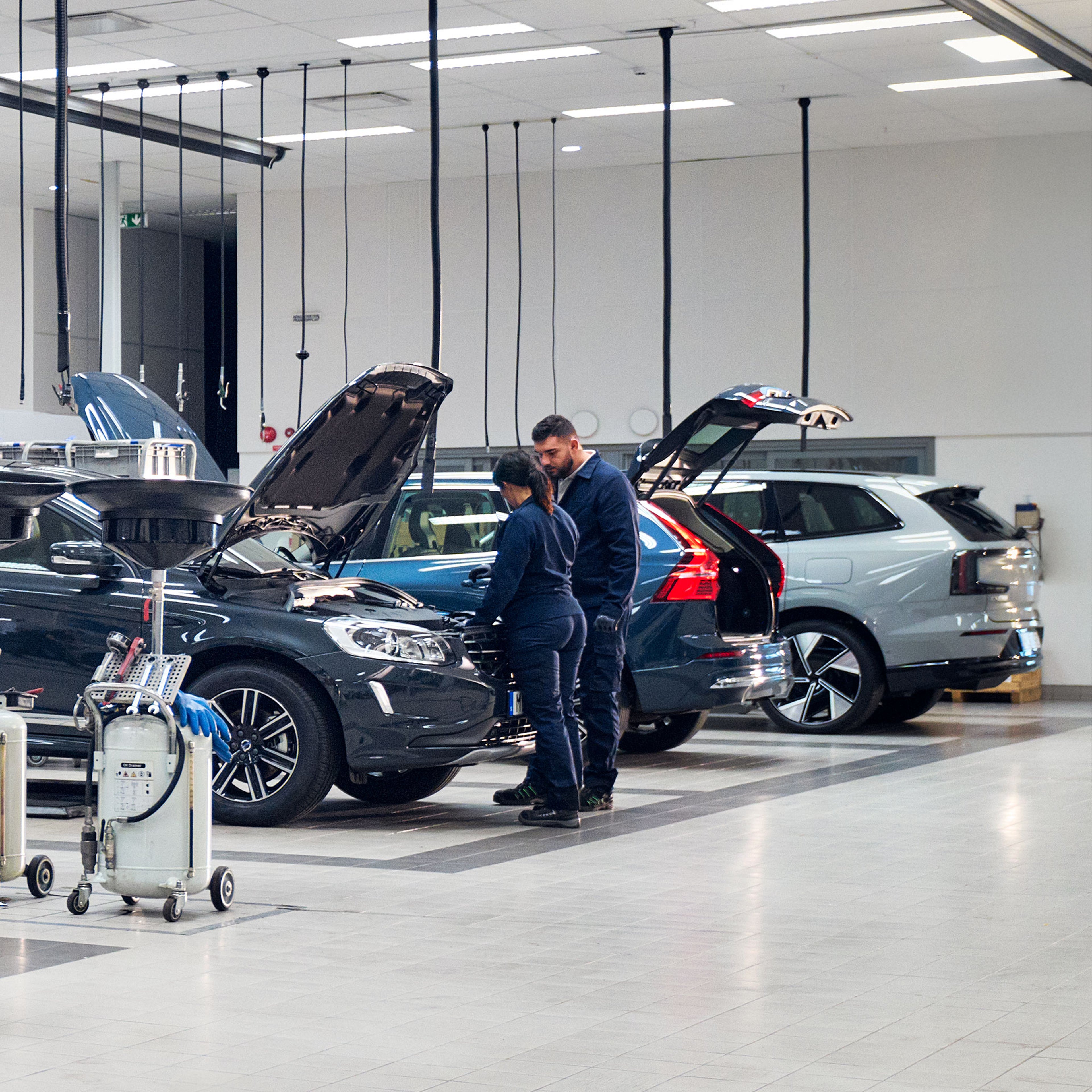 Kaksi Volvo Omamekaanikkoa tutkii huoltohallissa Volvo -autoa, jossa on konepelti auki.