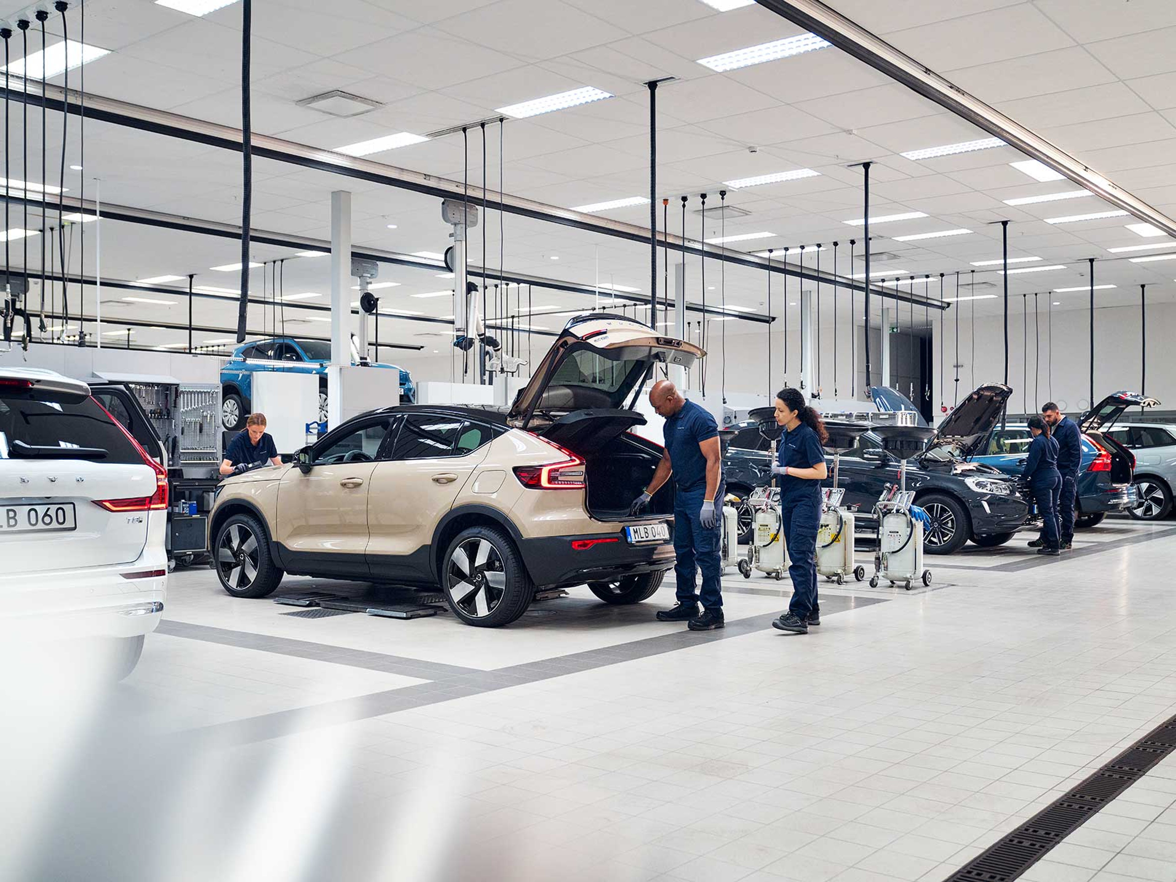 5 biler fra Volvo og teknikere der arbejder ved bilerne ses i et lyst værkstedsmiljø skråt bagfra.