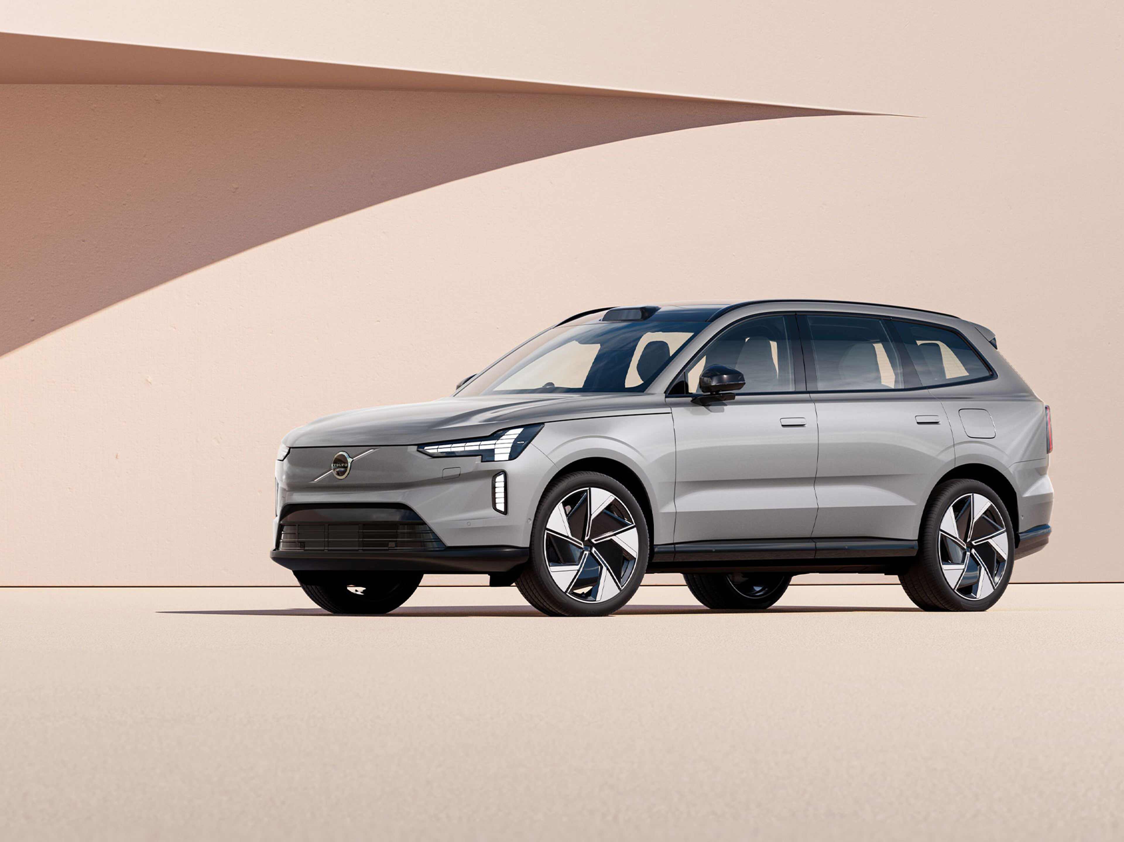 Volvo EX90 argenté garé devant un mur beige avec une ombre projetée