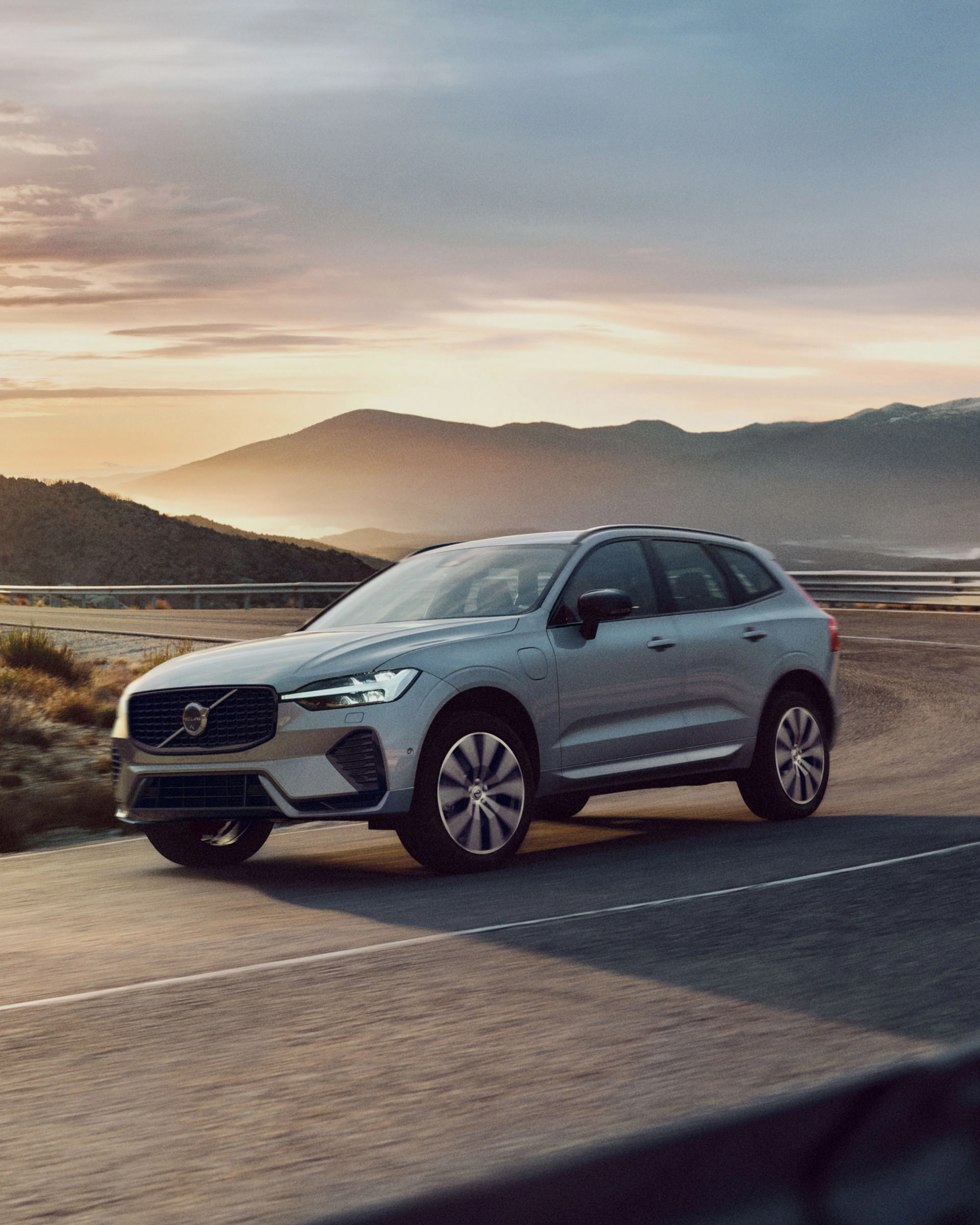 Ein XC60 fährt auf einer Straße entlang von Bergen. Im Hintergrund geht die Sonne auf.