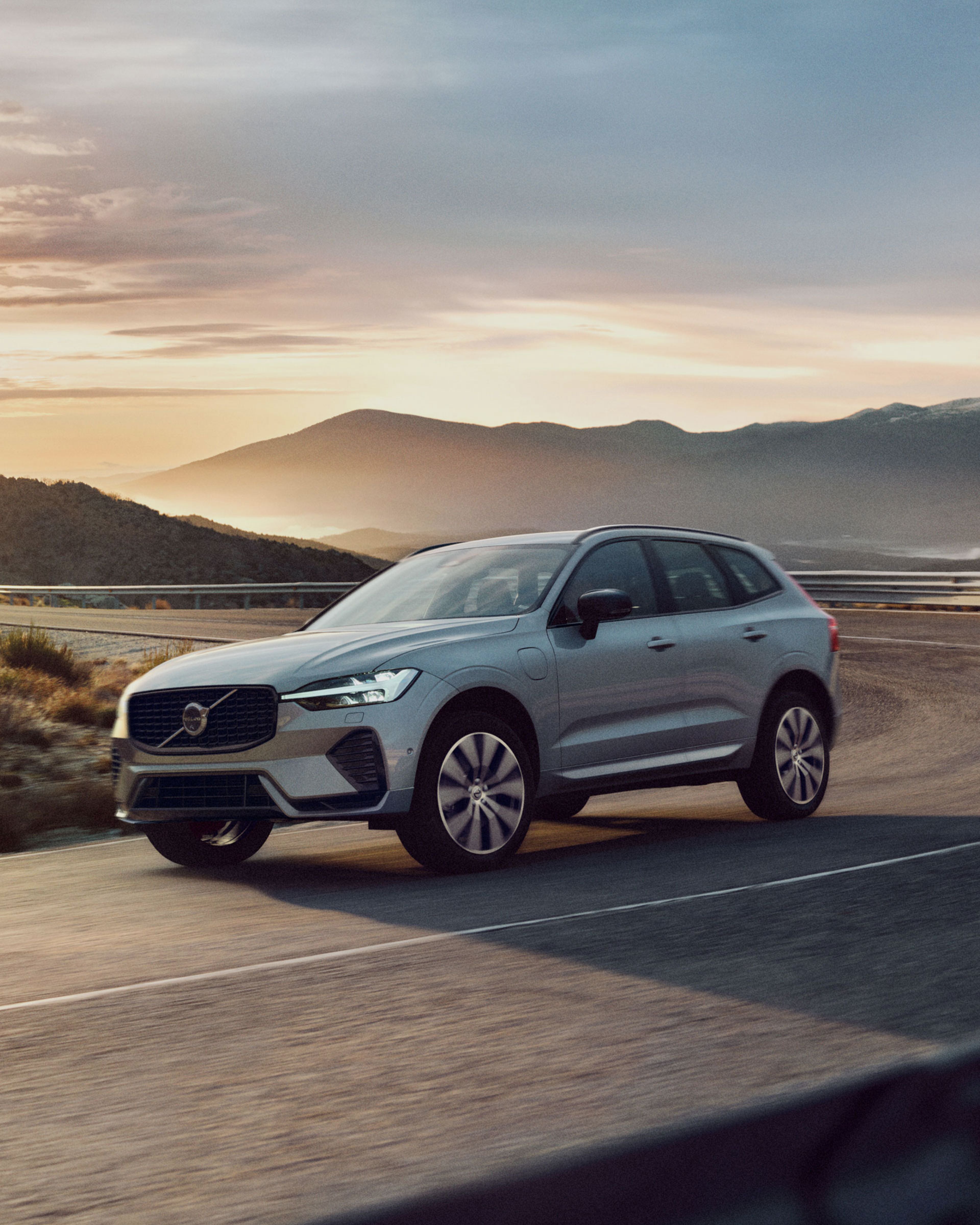 Ein XC60 fährt auf einer Straße entlang von Bergen. Im Hintergrund geht die Sonne auf.