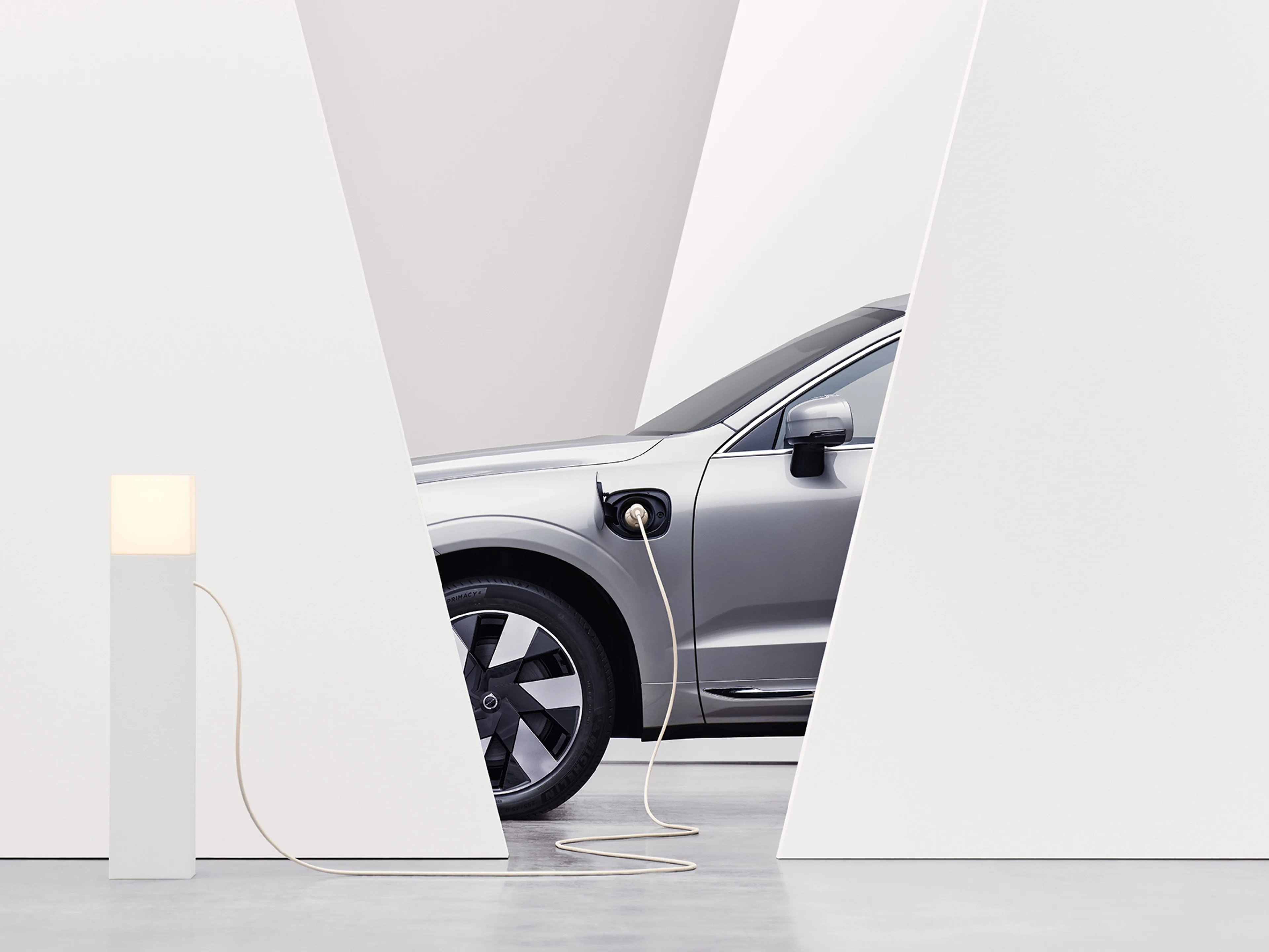 Une Volvo hybride rechargeable garée à une borne de recharge, branchée à un câble de recharge.
