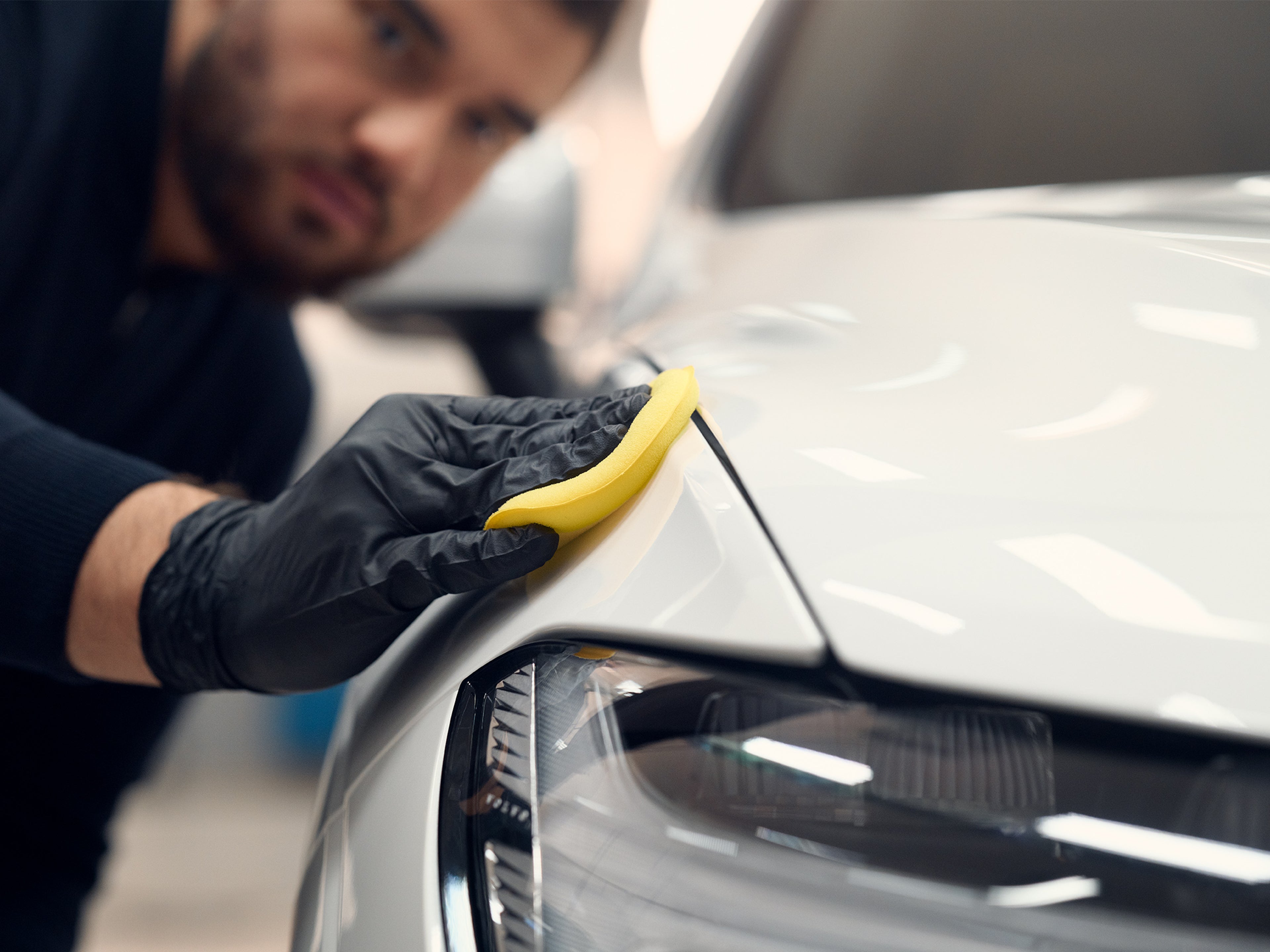 Volvo Omamekaanikko viimeistelee valkoisen Volvon oikean etulokasuojan vahausta.