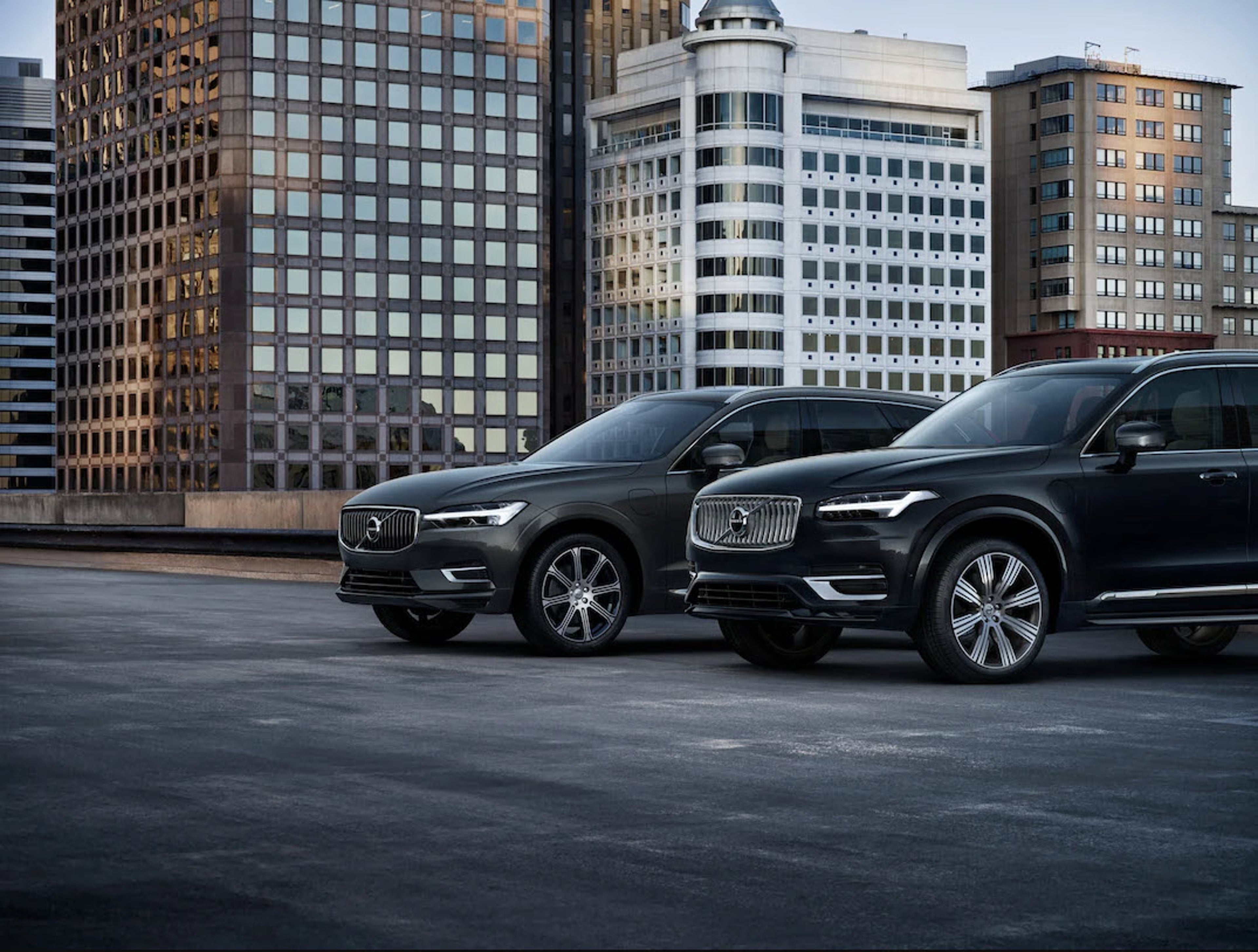 Mørk XC60 og XC90 parkert på ett tak med bygninger bak