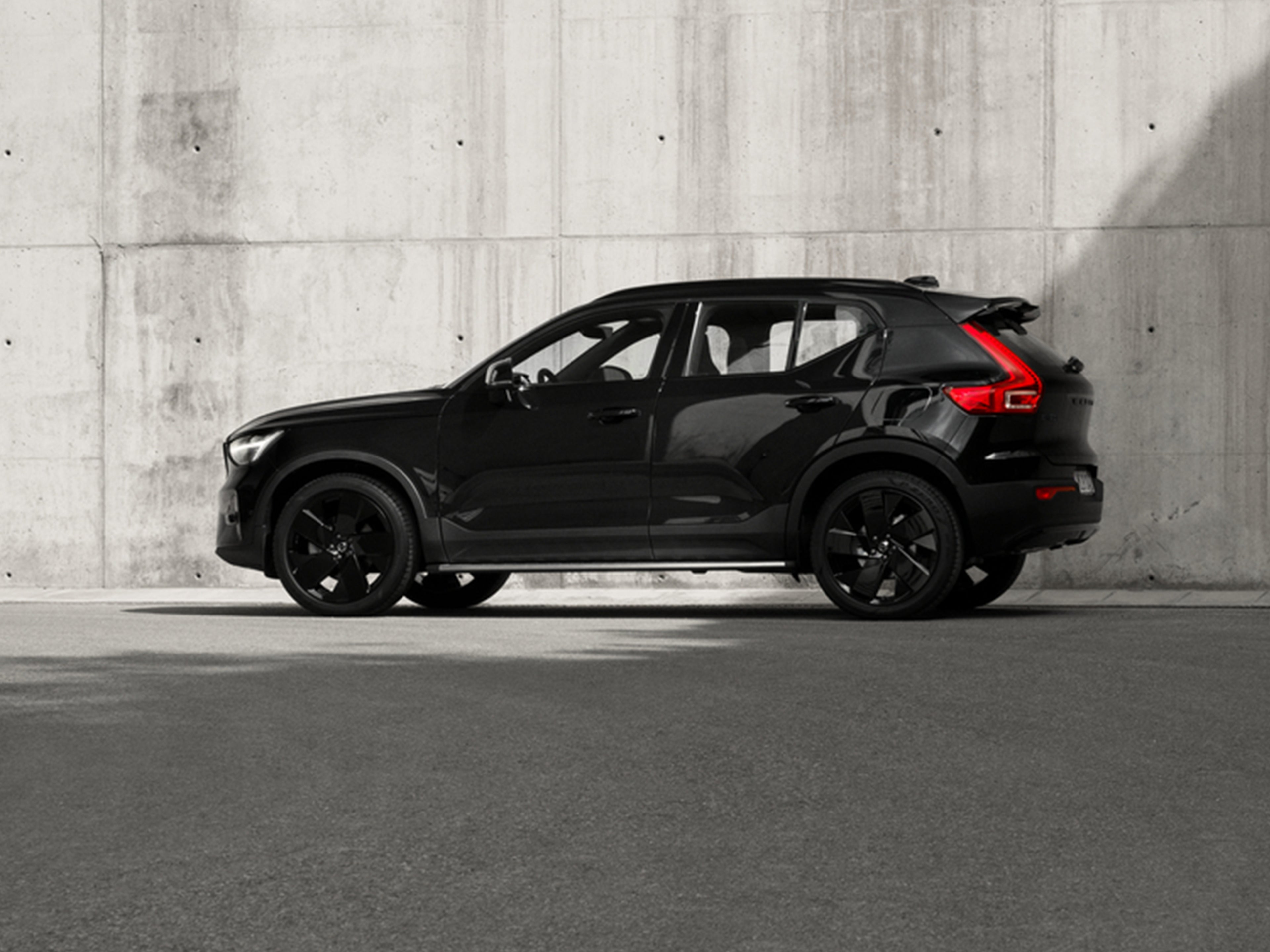 Volvo EX40 Black Edition täyssähköinen katumaasturi kuvattuna sivusta betoniseinää vasten.