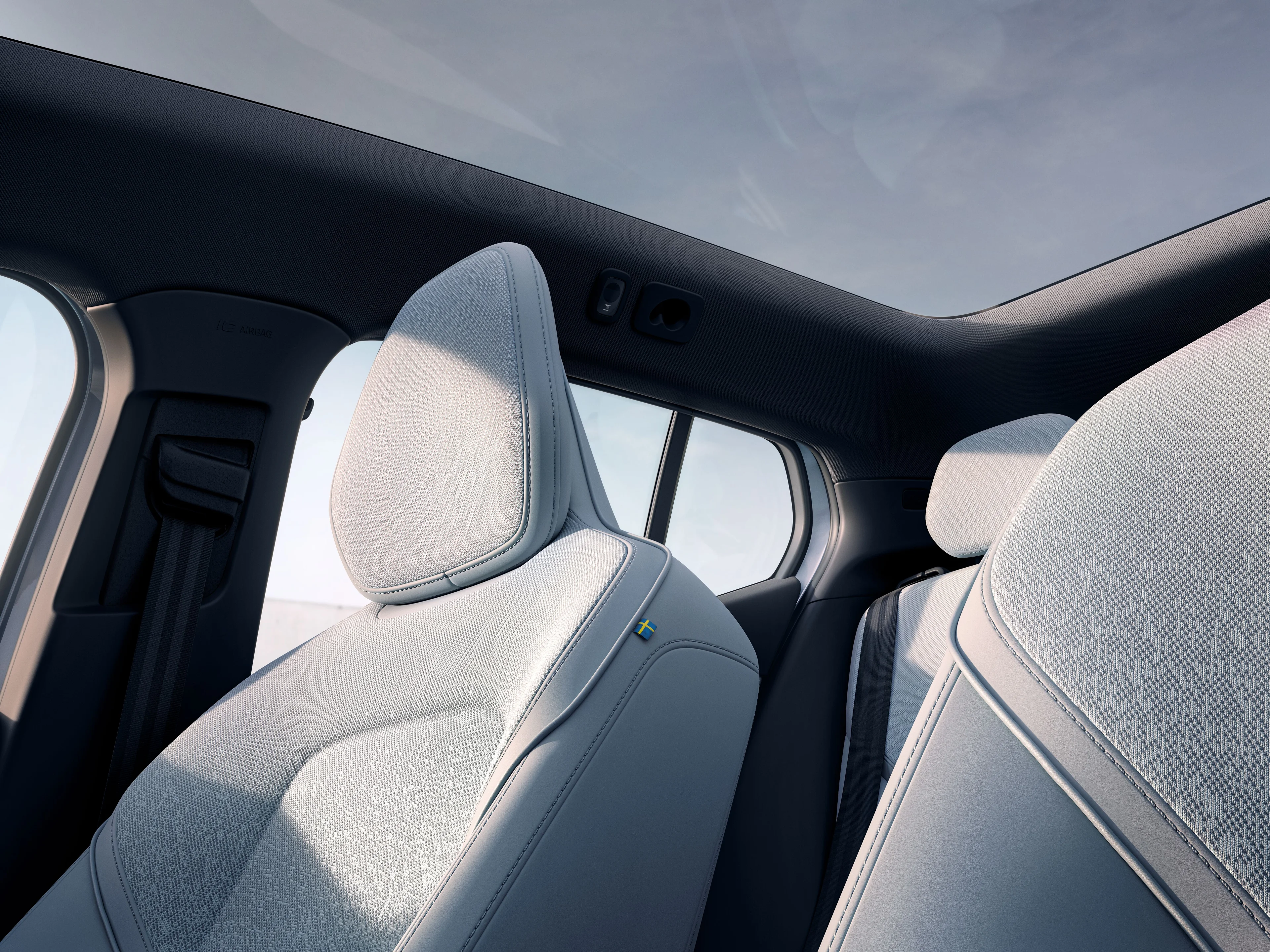 Intérieur d’une voiture Volvo avec sièges gris clair et toit panoramique laissant voir le ciel bleu.